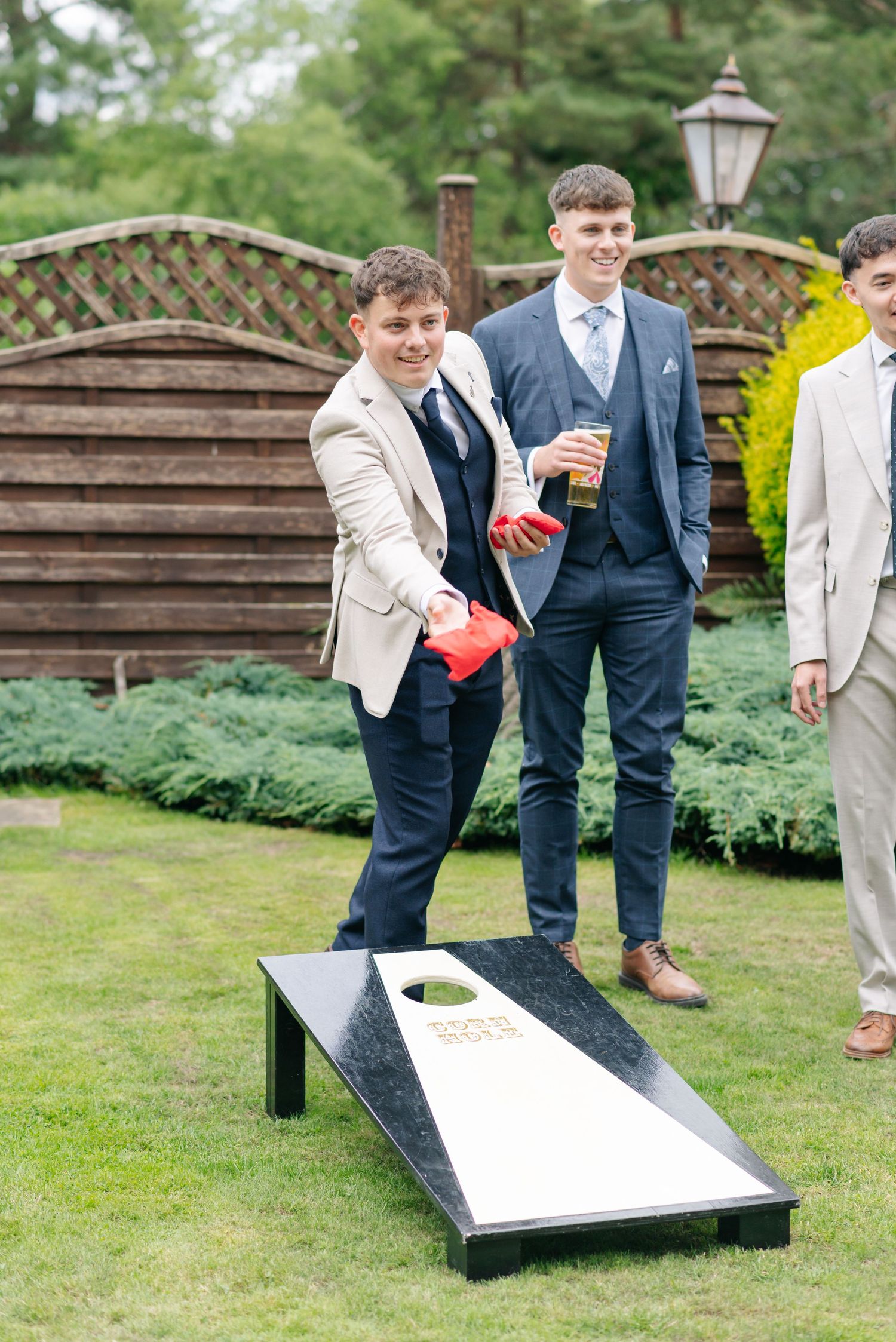 Wedding guests playing cornhole lawn game at an outdoor reception.