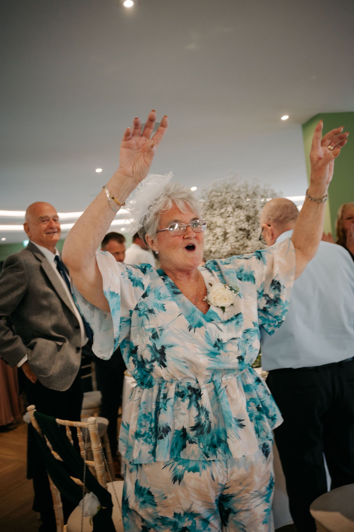 Wedding guests dancing enthusiastically at a reception with floral decorations in the background.