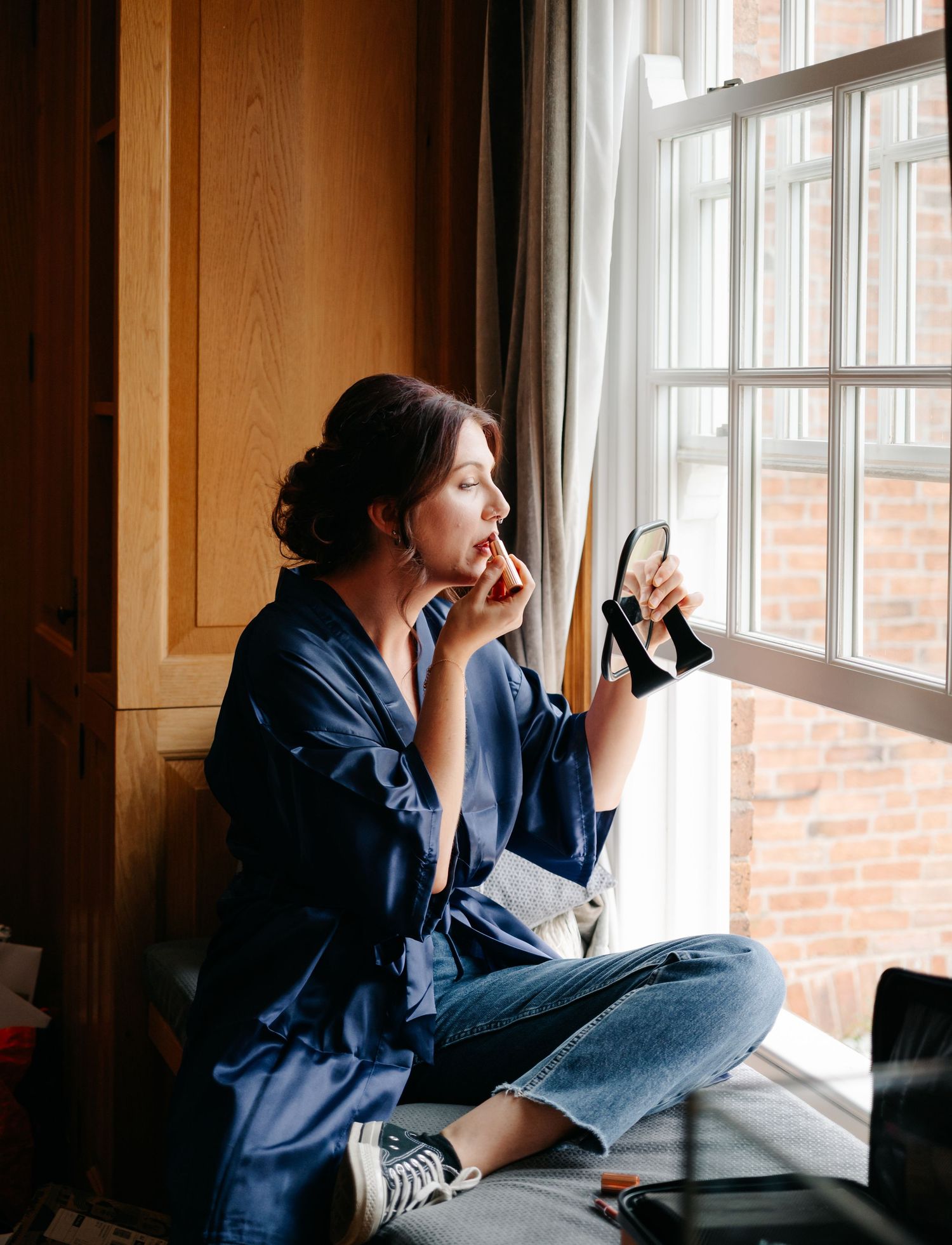 Woman in denim and navy shirt sits cross-legged by bright window in series of pensive candid poses.
