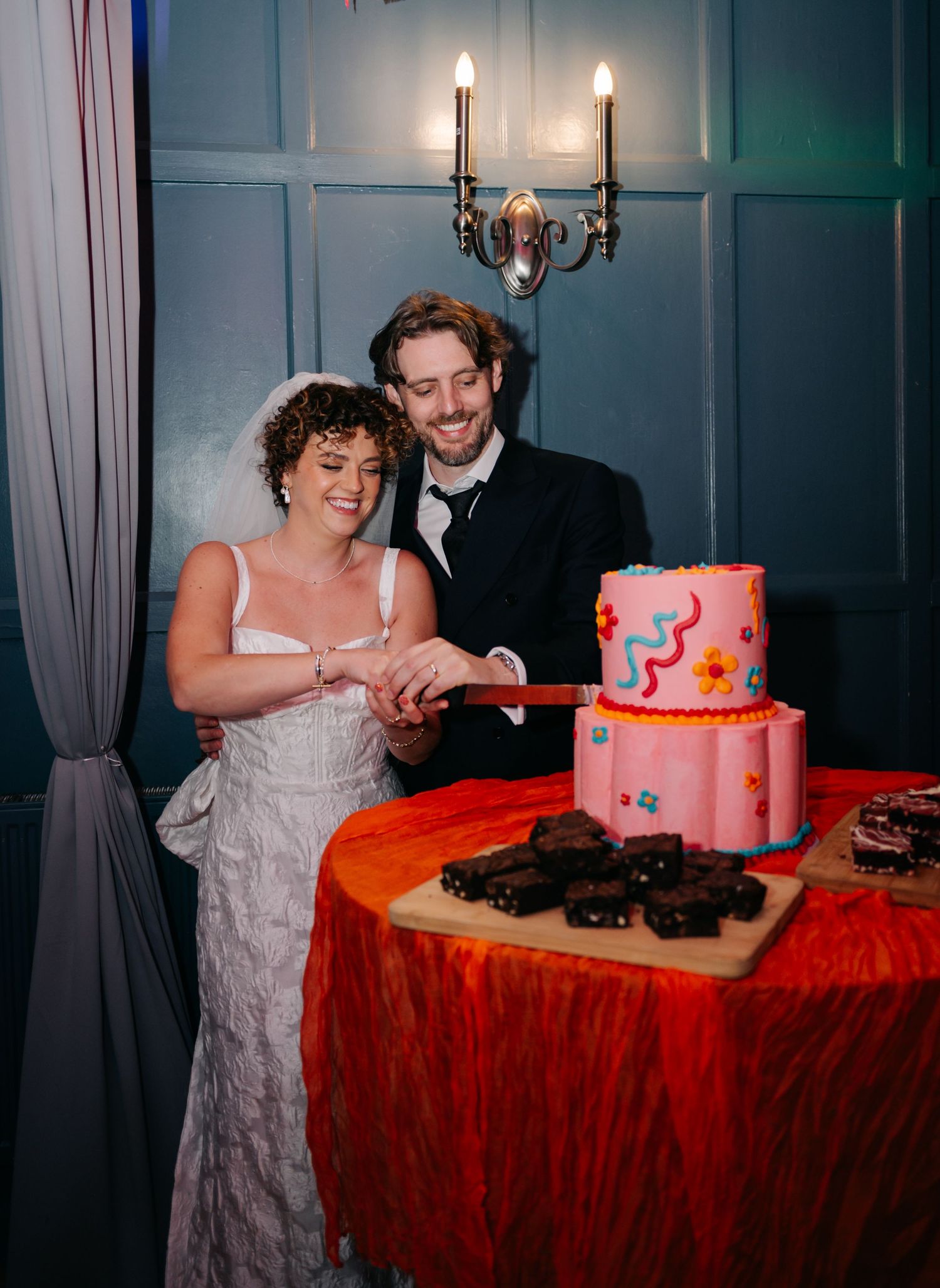 Wedding couple cutting their pink and coral tiered cake at reception.