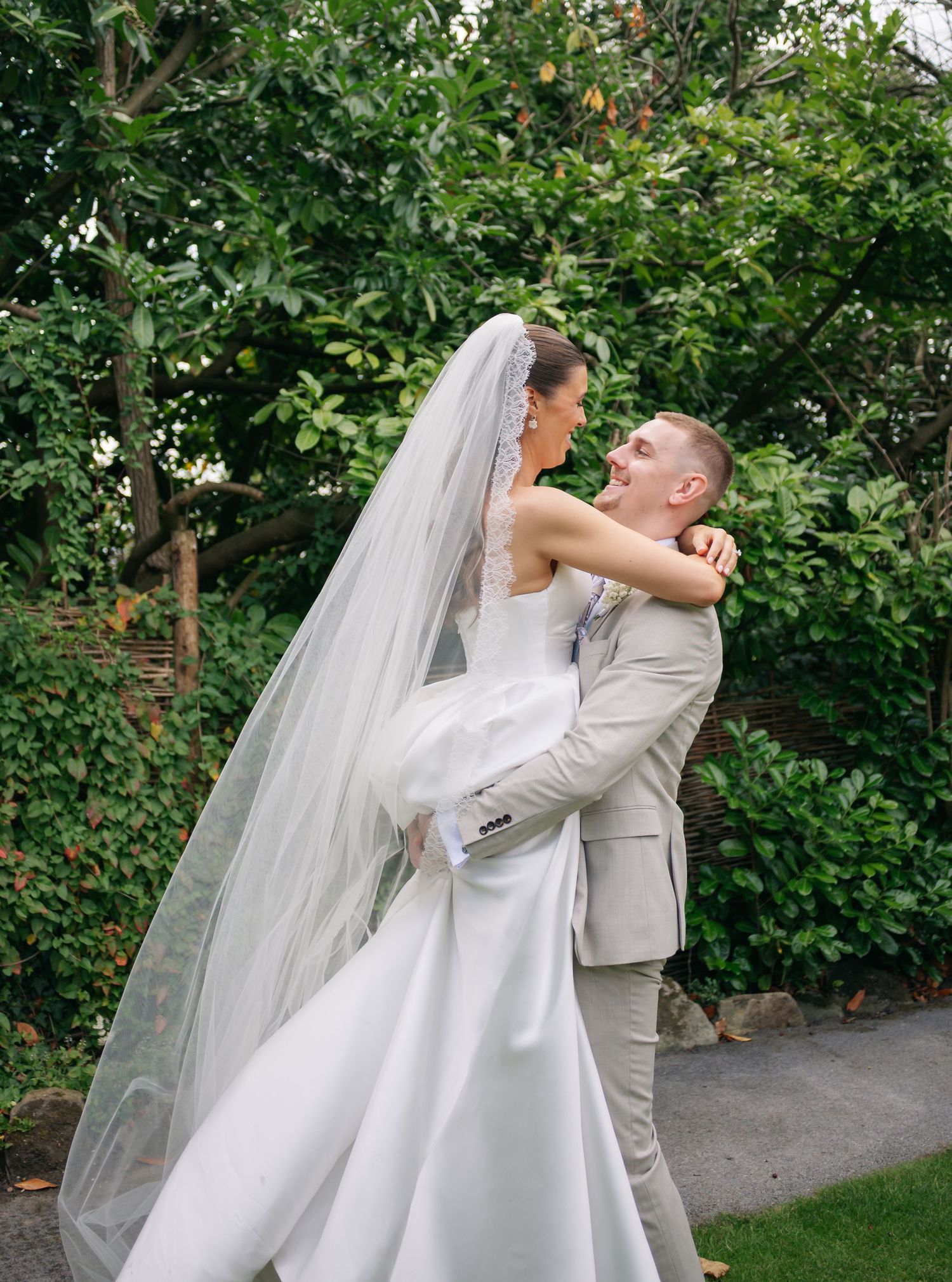 A romantic wedding couple embraces in a garden setting with lush greenery.