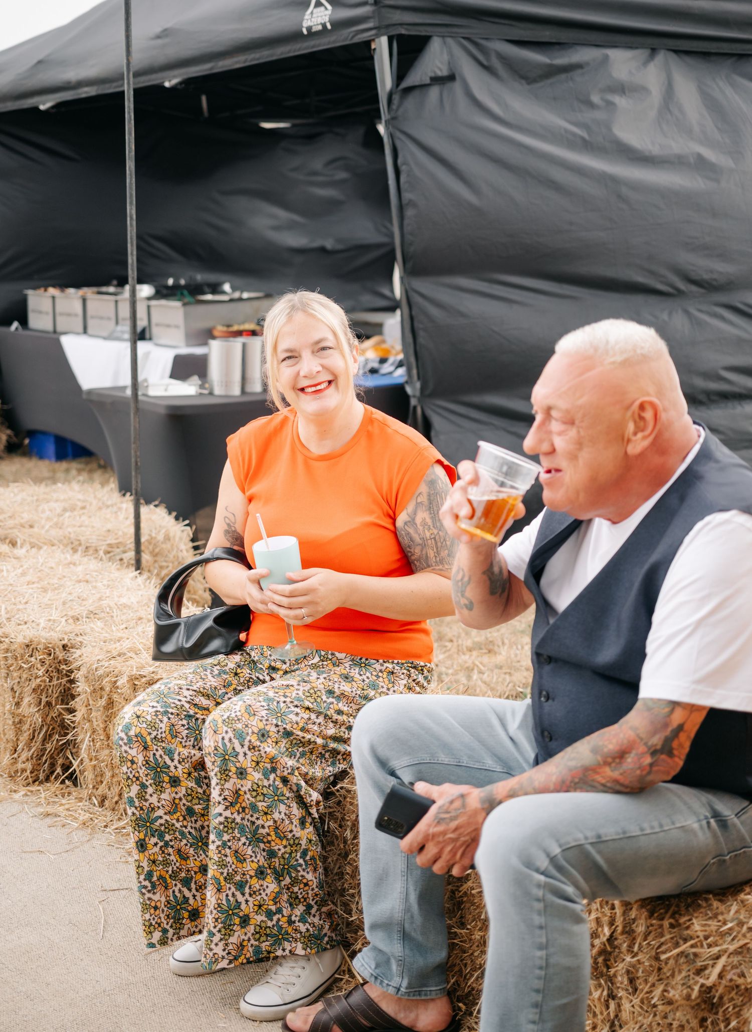 Wedding guests relaxing on hay bales under a black tent canopy.