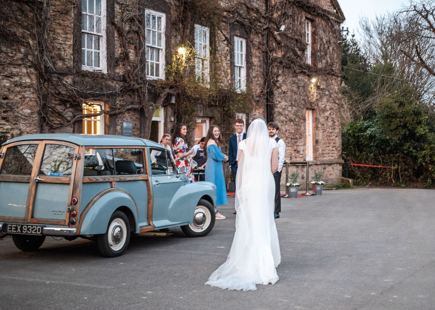 A vintage blue car parked outside a rustic stone building during a wedding celebration.