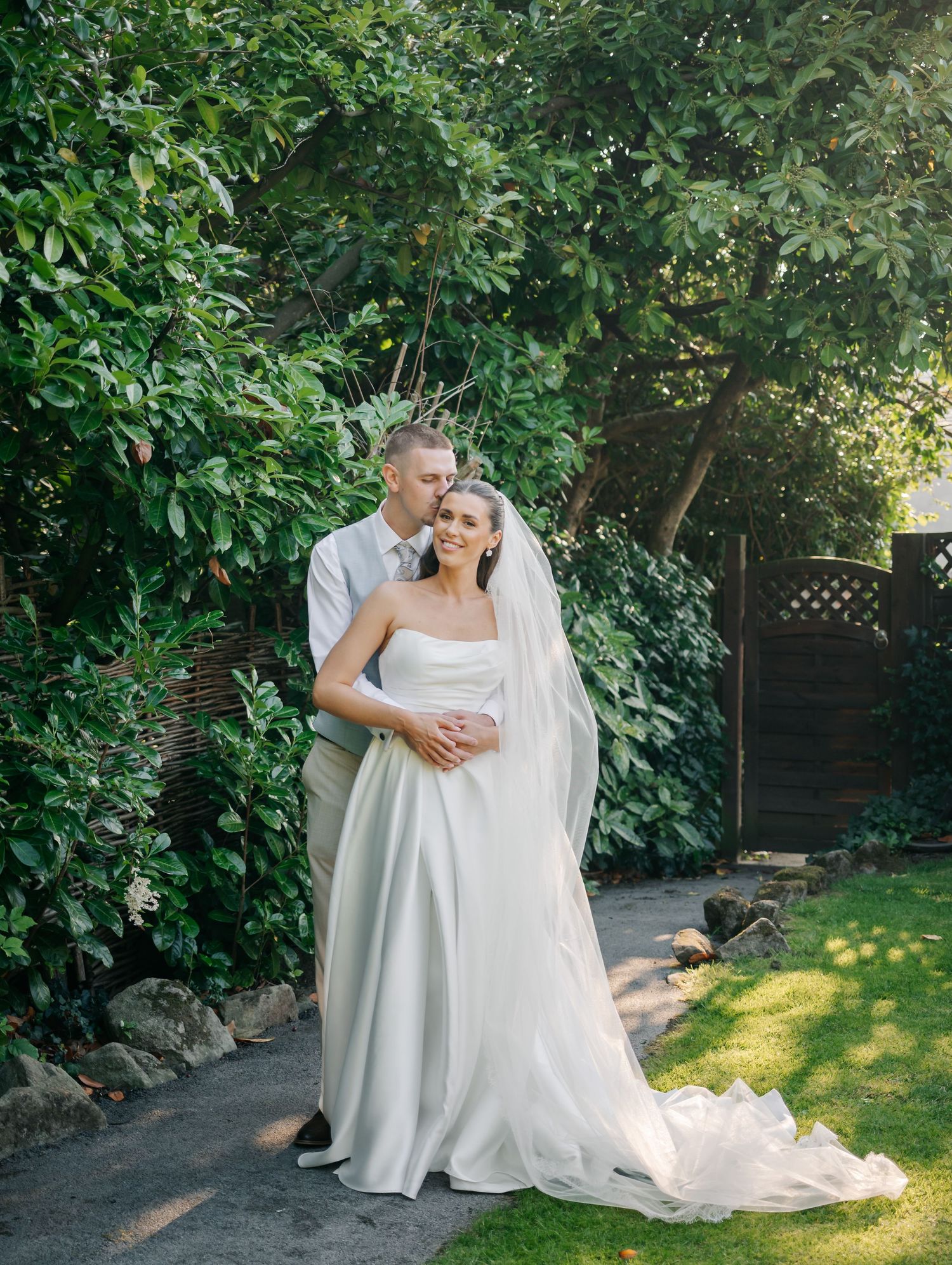 Wedding couple embracing in a sunlit garden with lush greenery backdrop.