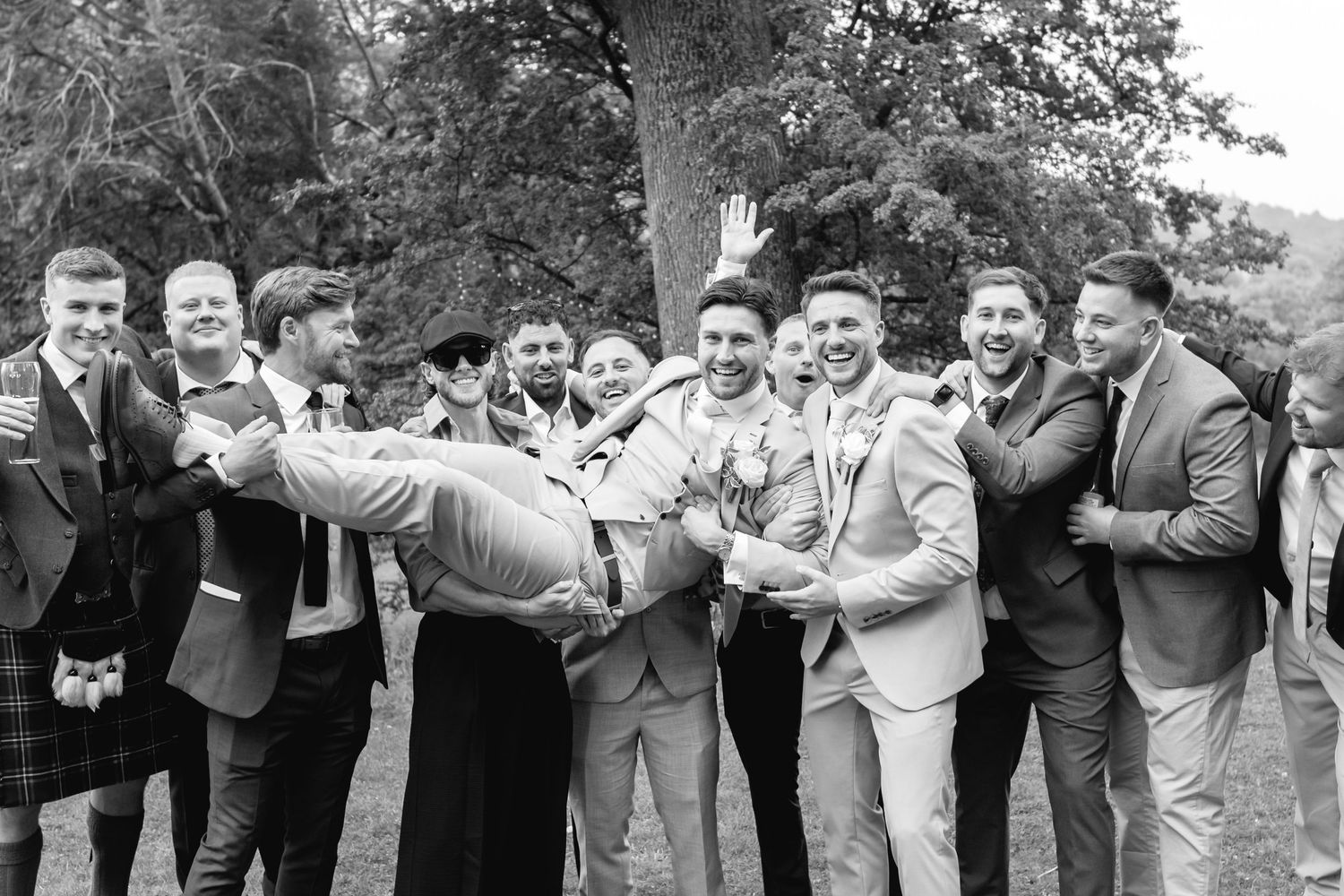 Groomsmen in gray suits laughing together at outdoor wedding celebration.