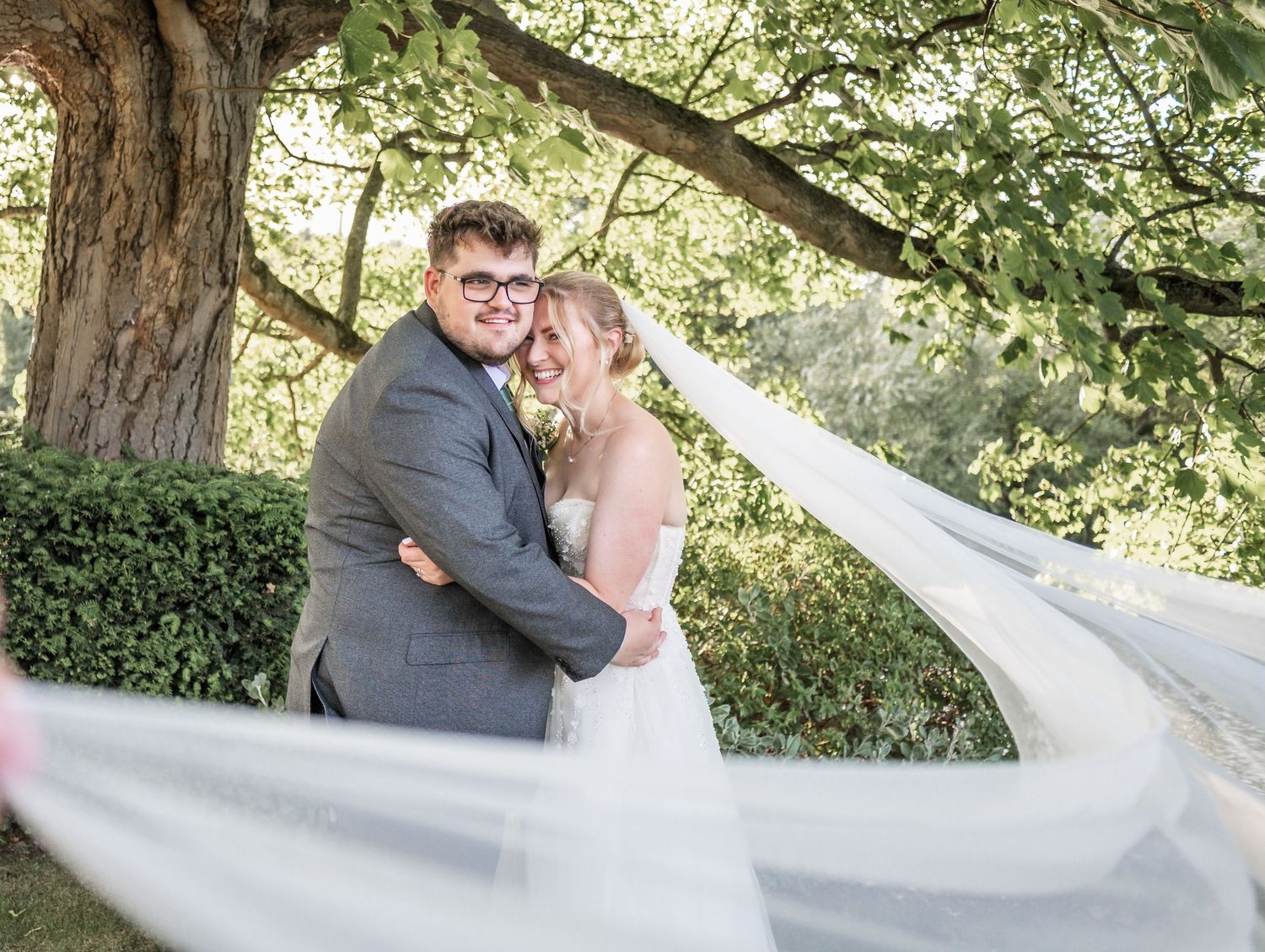 Romantic wedding portrait with flowing veil under ancient tree branches.