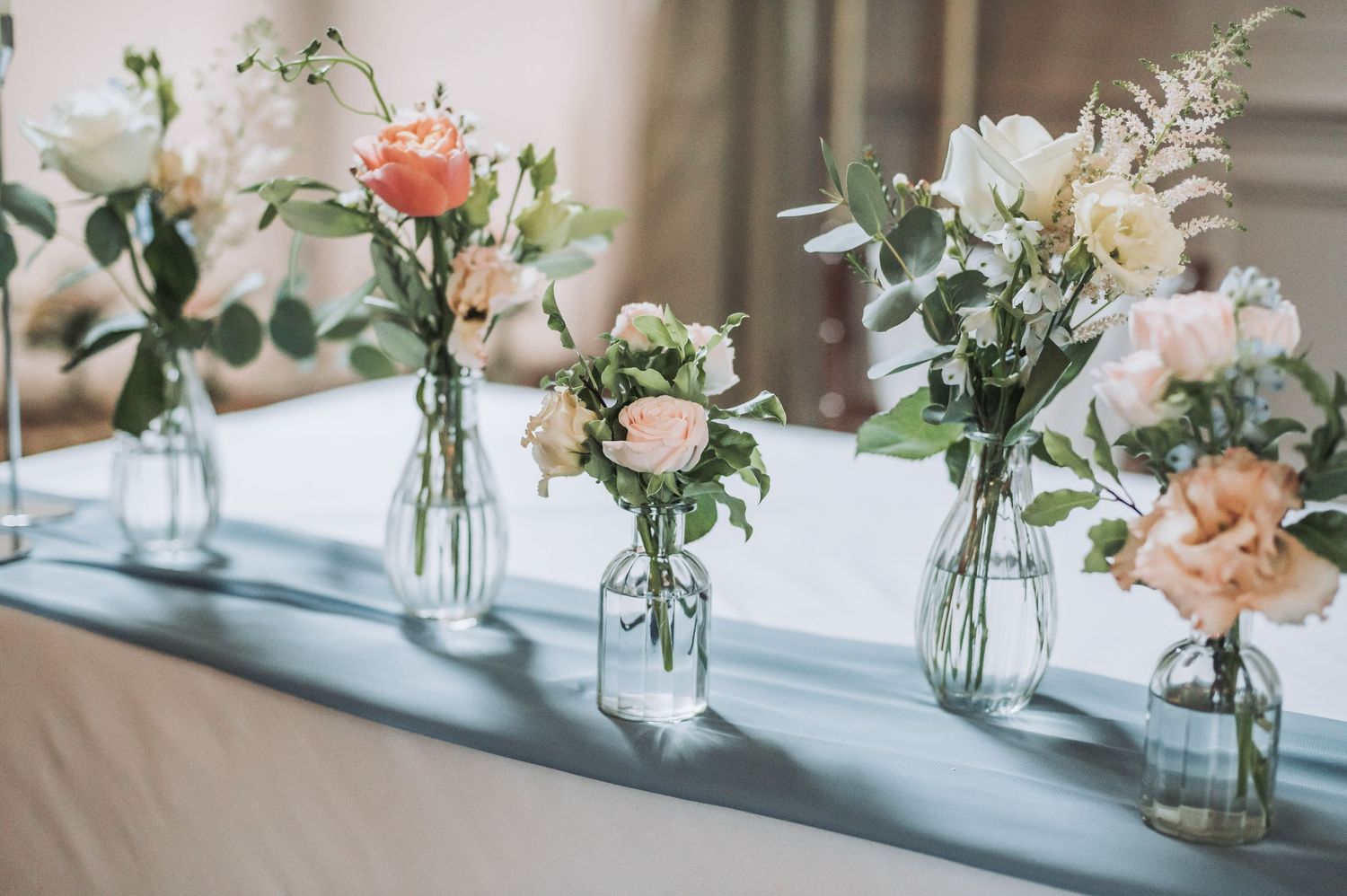 Elegant wedding centerpieces with pink roses and greenery in clear glass vases.