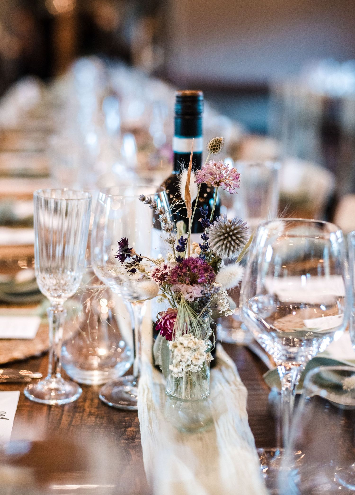 Intimate table setting with wildflower arrangements in small glass bottles and wine glasses.