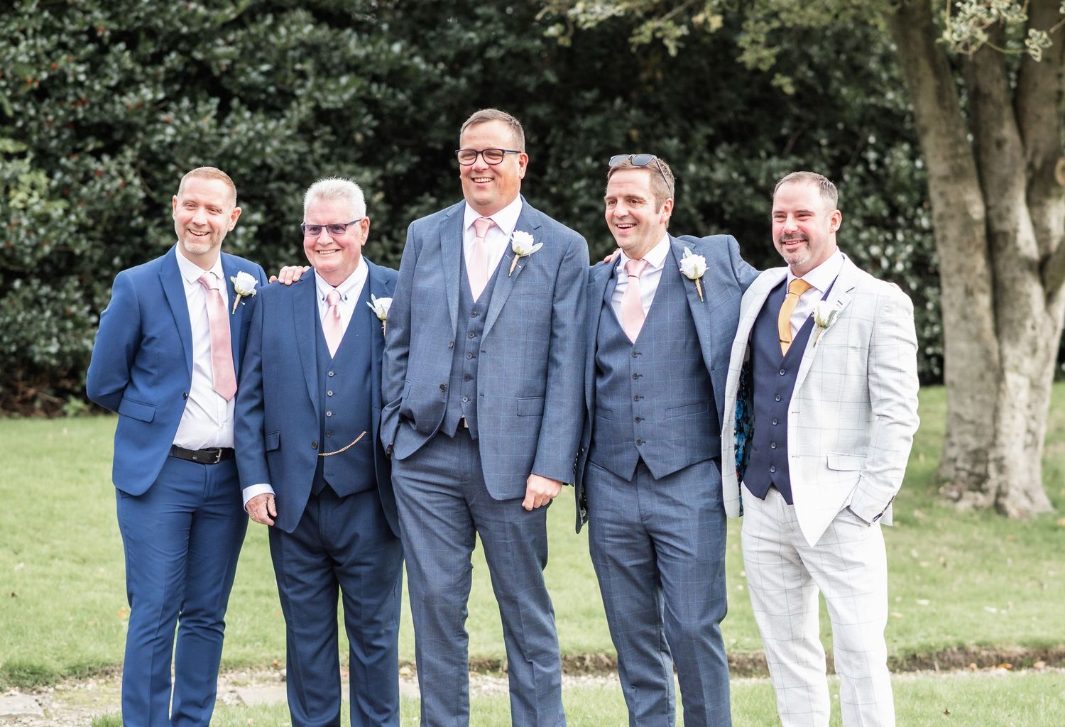 Group photo of five groomsmen in blue and grey suits standing outdoors.