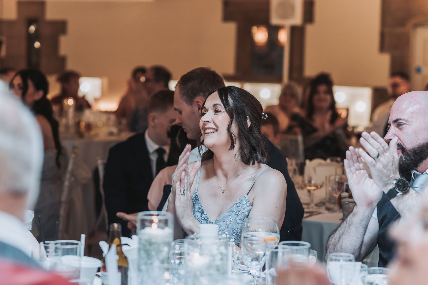 A guest in a blue dress smiles warmly during a wedding reception.