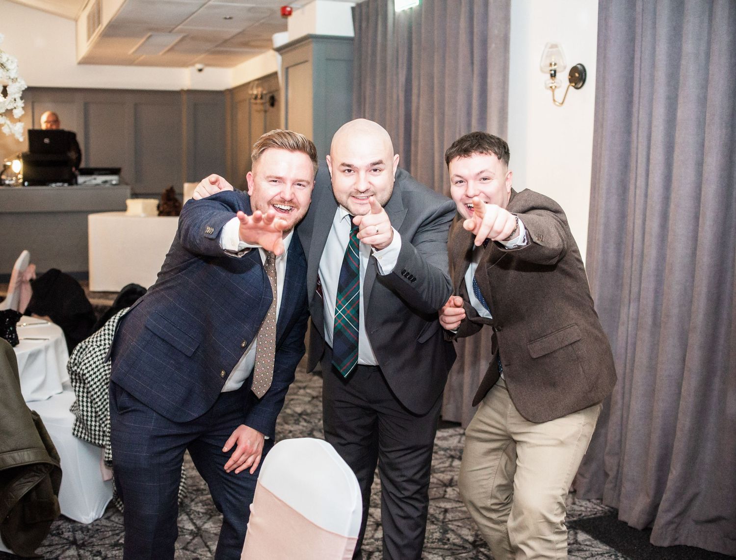 Three guests strike playful poses at a wedding reception in formal attire.