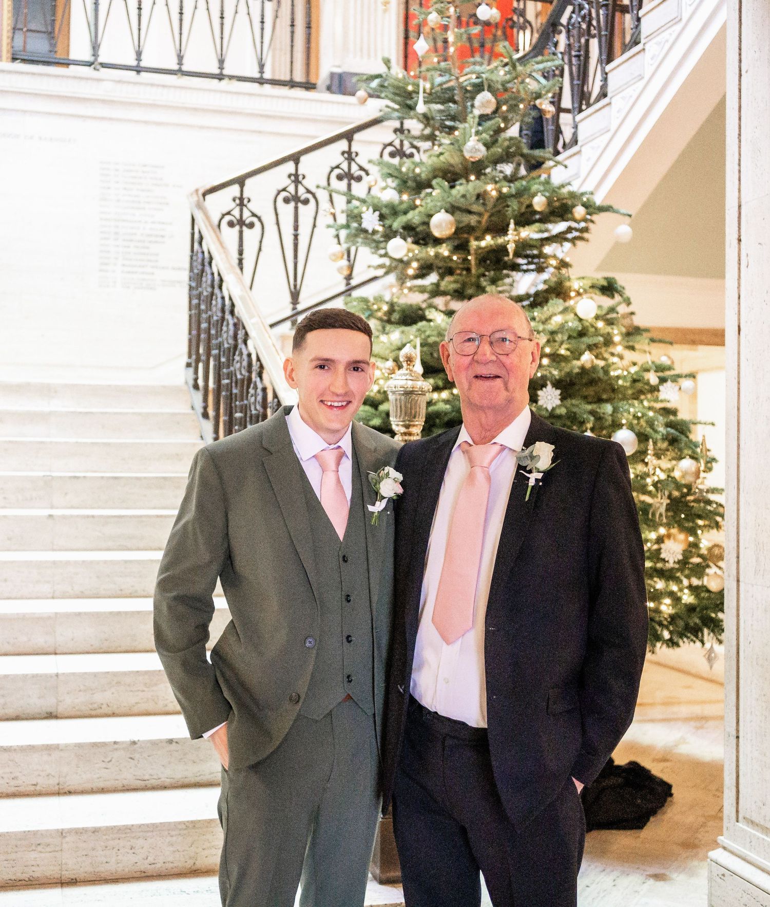 A festive Christmas scene on white stairs with a decorated tree and formal-dressed guests.