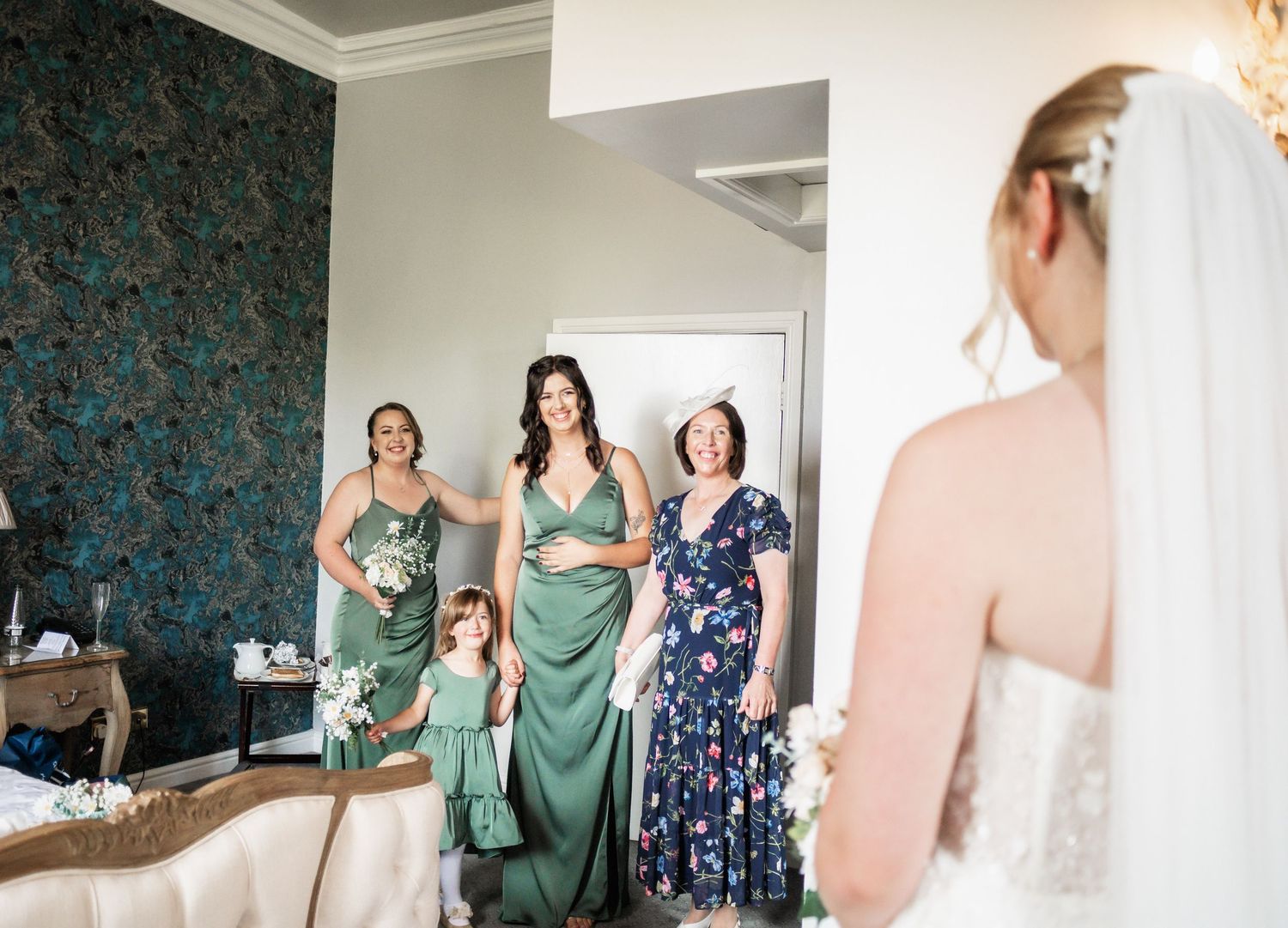 Bridesmaids in green dresses watch emotional getting ready moment in elegant dressing room.