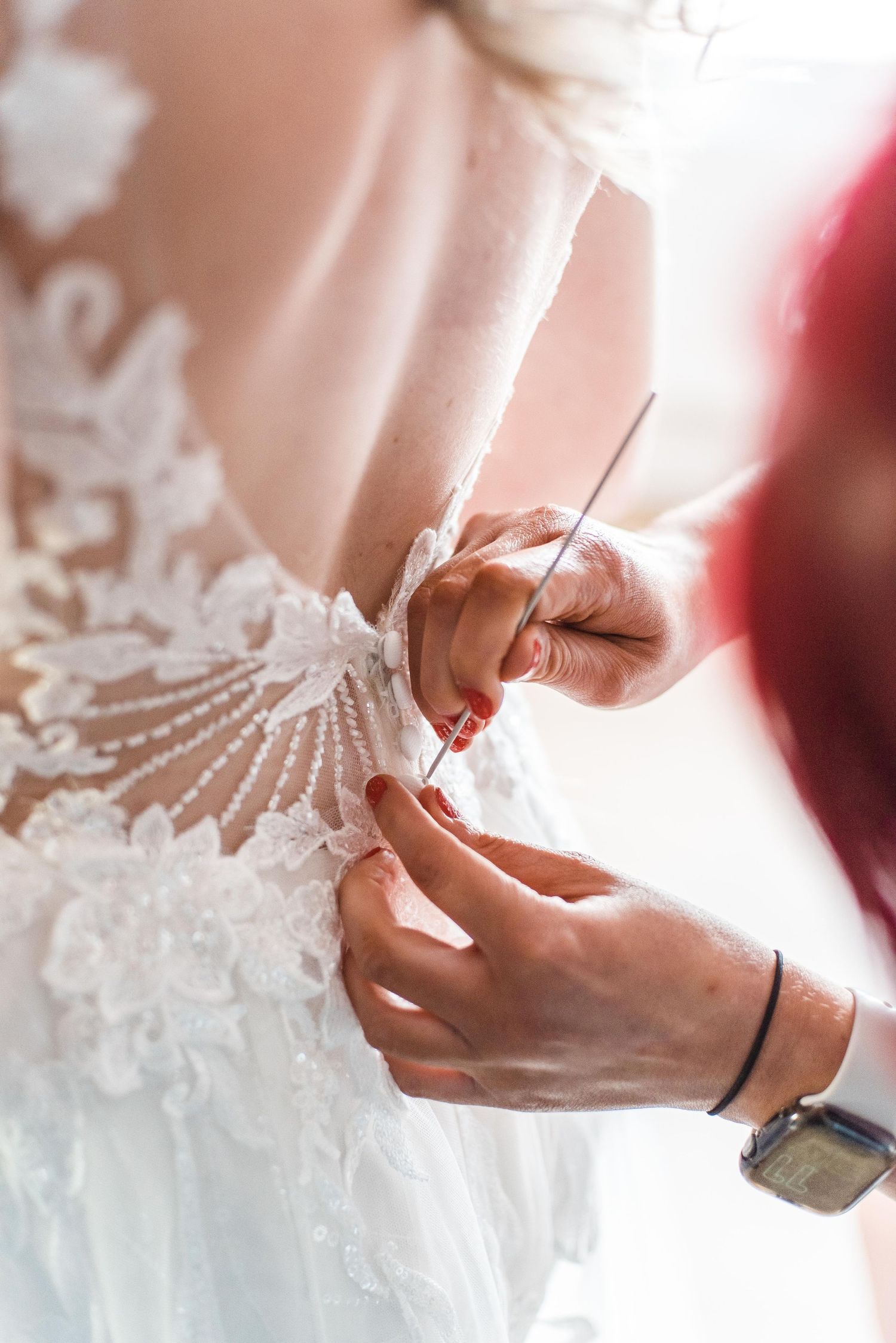 Close up of hands adjusting delicate lace details on a white wedding dress.