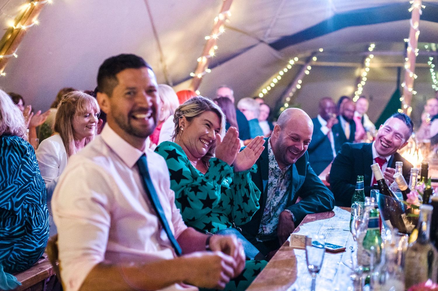 Wedding guests enjoying a lively reception under a tent with string lights.