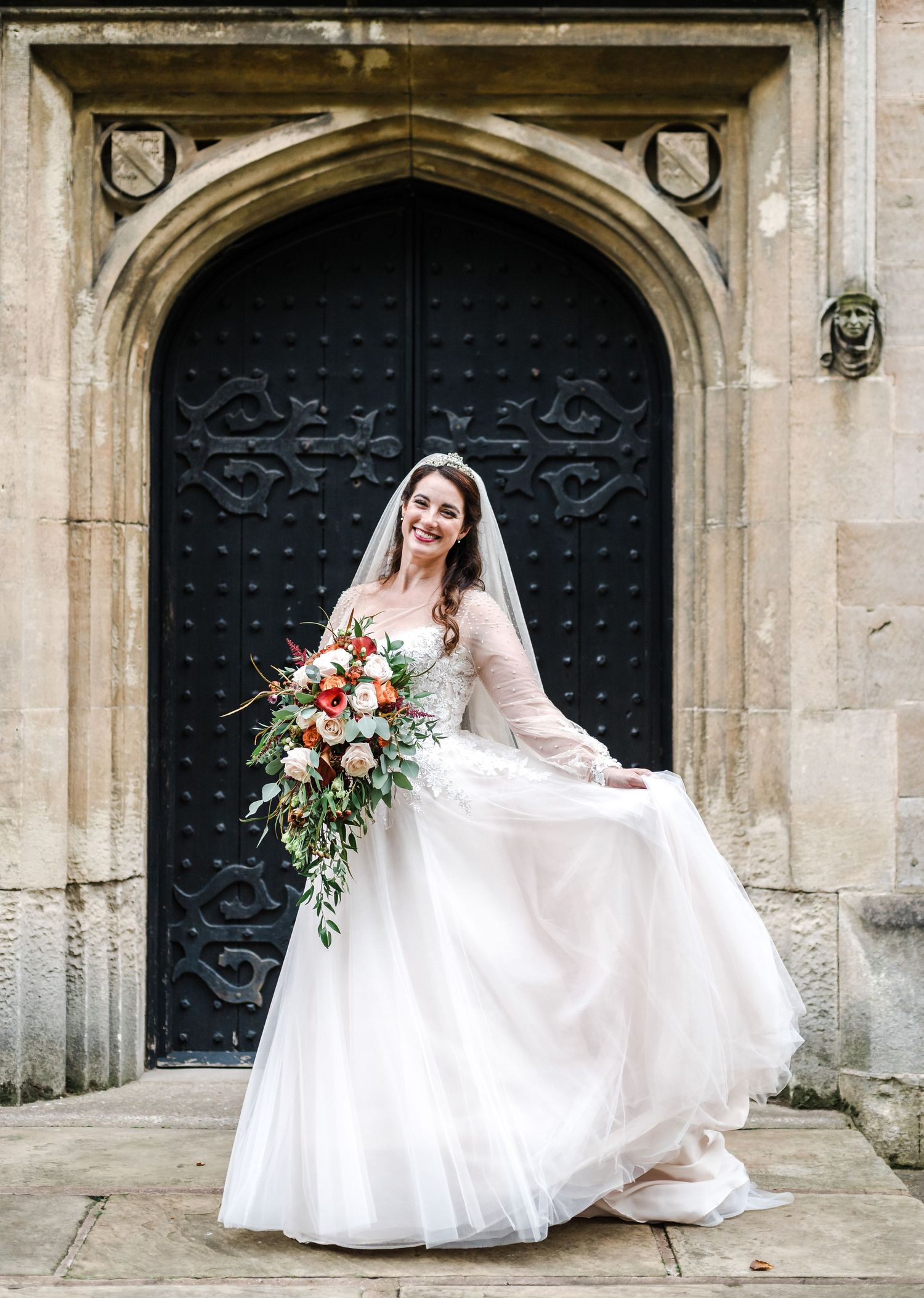 Bride in flowing white dress poses against ornate black church door.