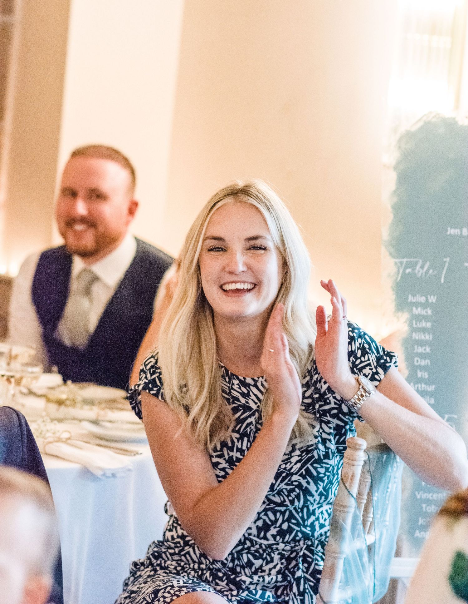 A guest laughs joyfully during a wedding reception, wearing a patterned black and white dress.