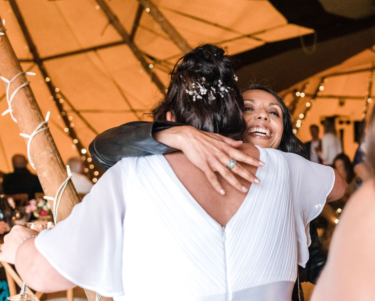 Emotional embrace at a wedding reception under warm-lit tent with string lights.