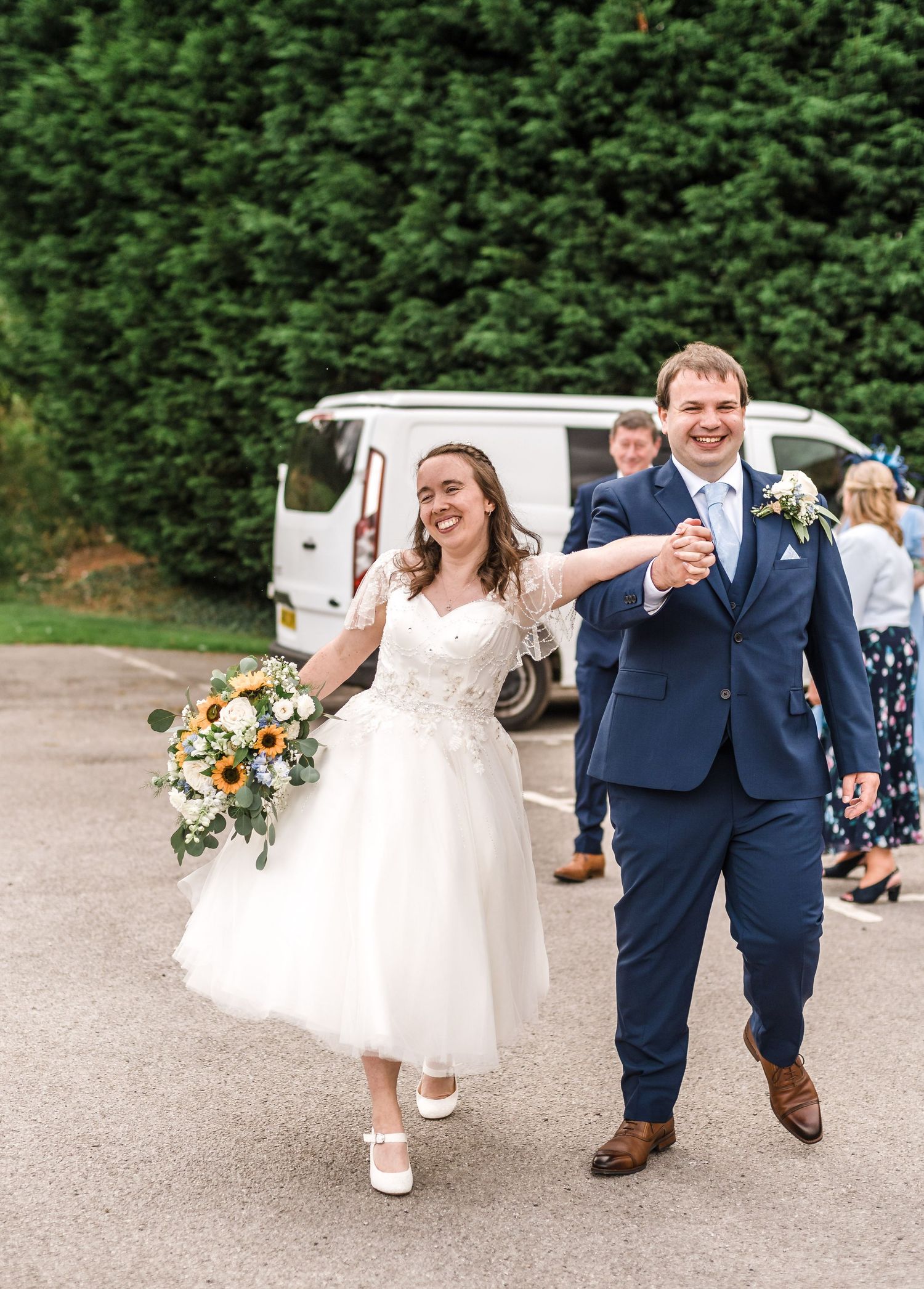 Newlyweds walking and laughing together outdoors with white van in background.