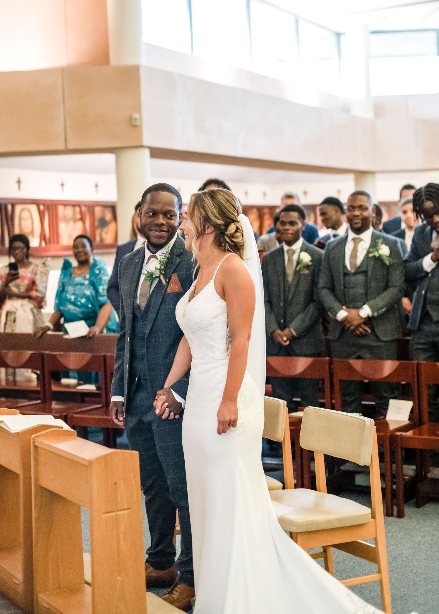 A couple stands at the altar during their wedding ceremony surrounded by attendants in a church setting.