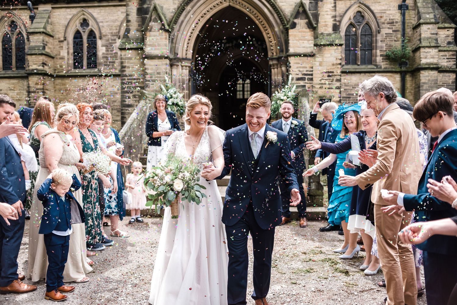 Wedding celebration outside a beautiful gothic stone church with guests throwing confetti.