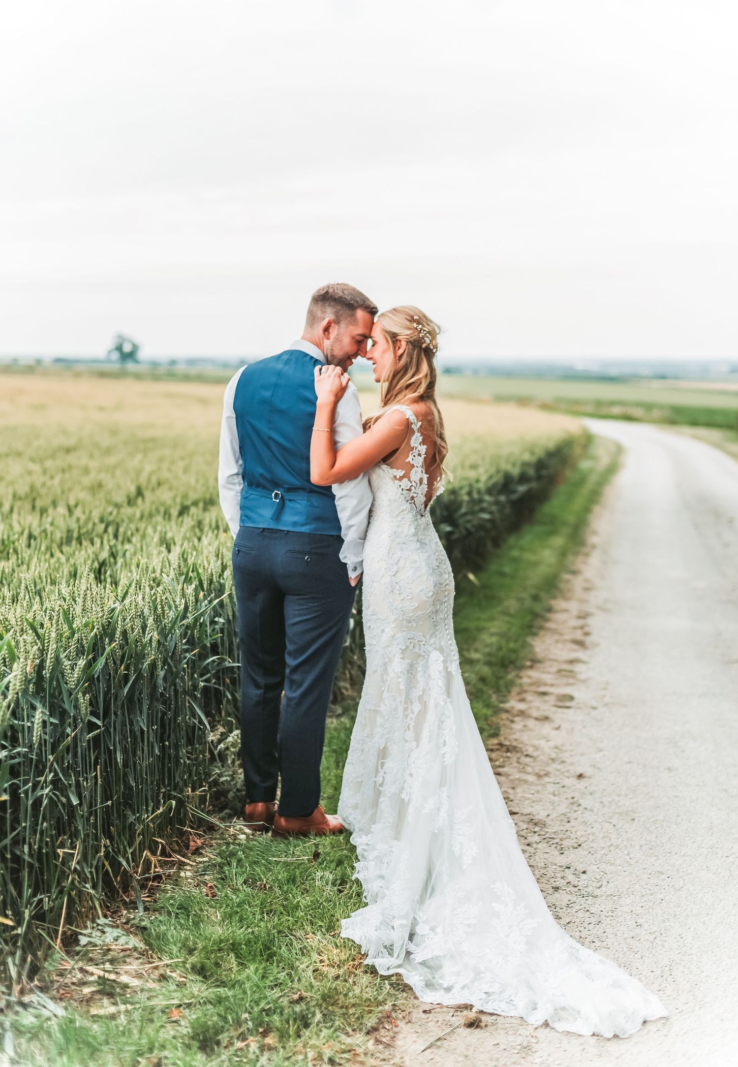 Couple shares intimate moment on country road beside wheat field.