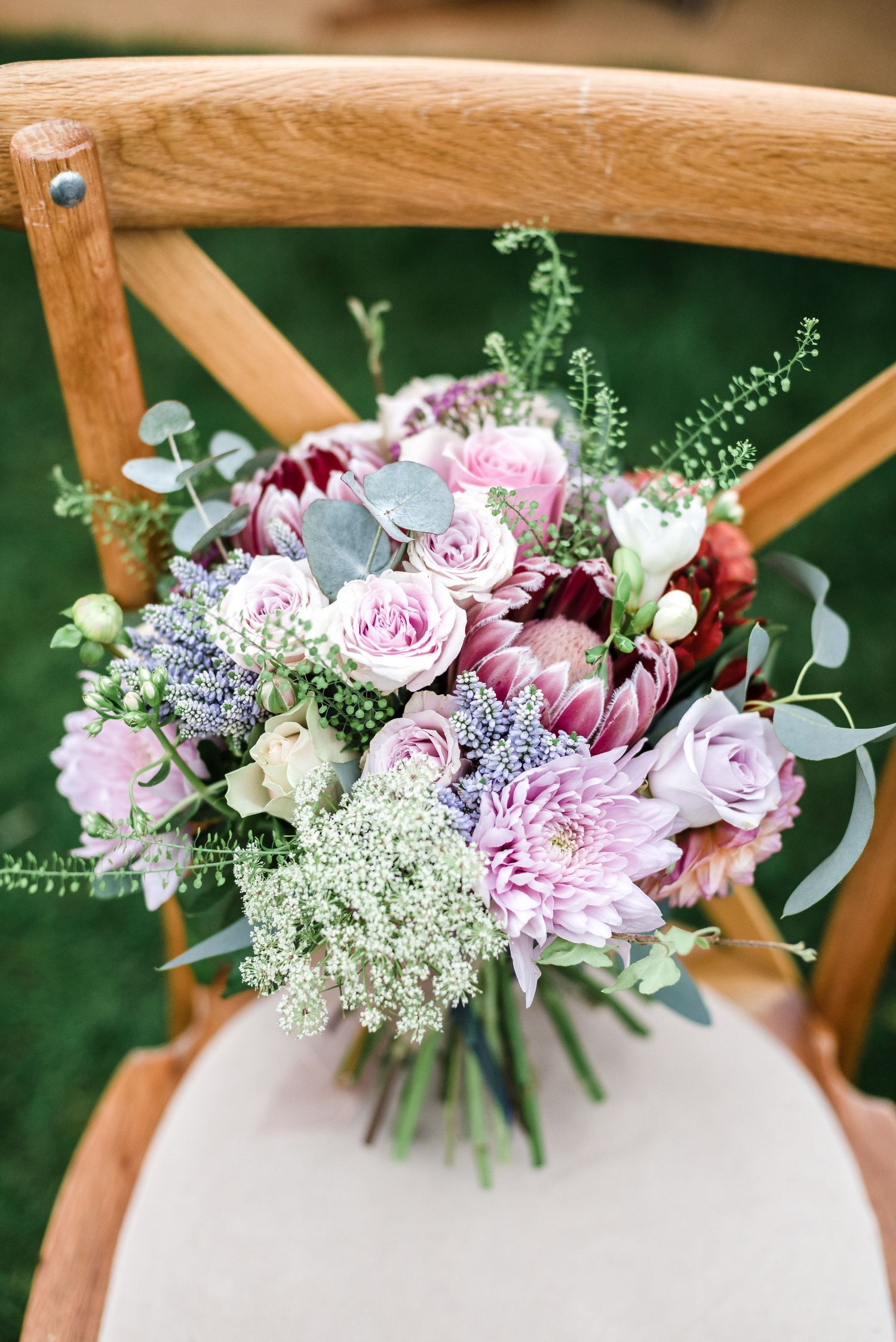 Delicate pink and purple floral bouquet arranged on a wooden crossback chair.