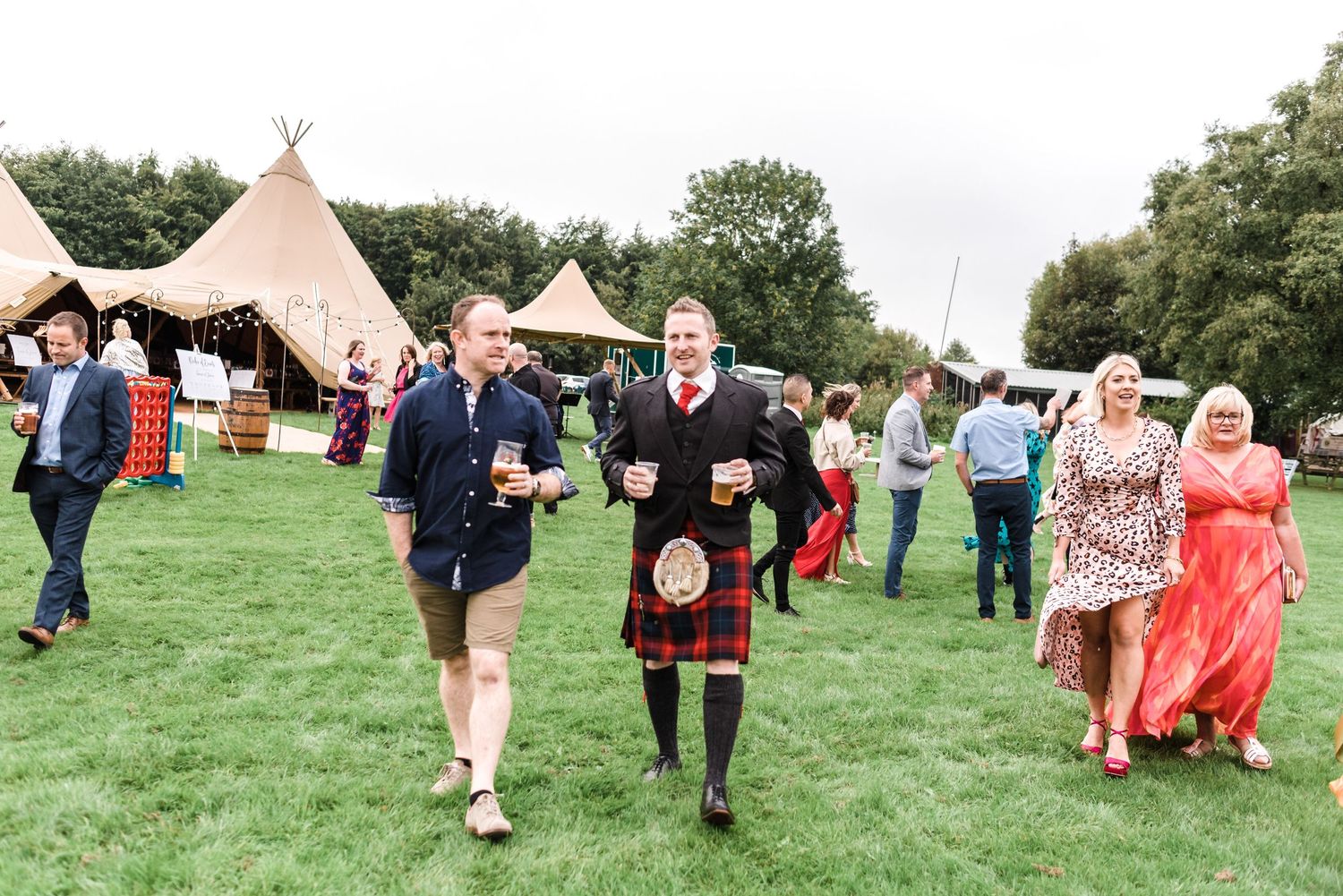Guests walking across a grassy field with teepee tents in the background at an outdoor event.