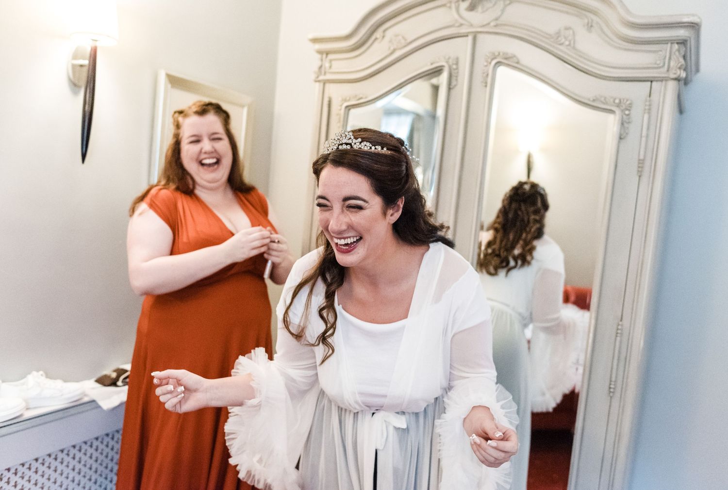Candid moment of joy and laughter during wedding preparations in a white decorated room.