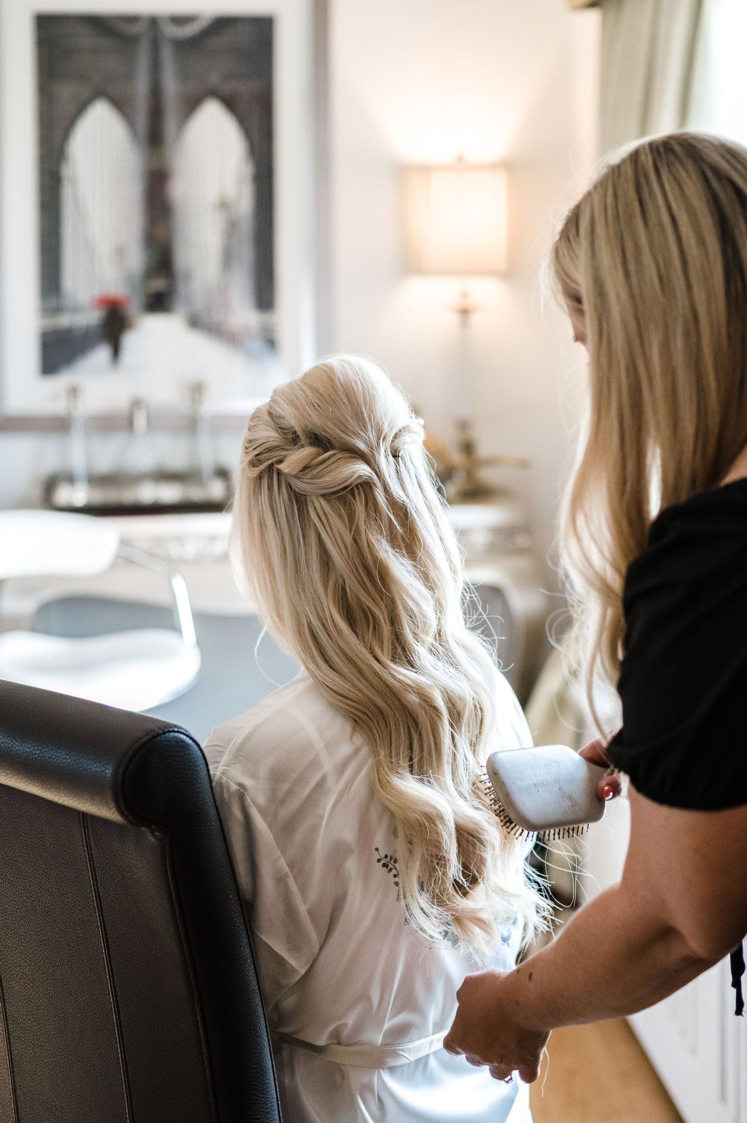 Hairstylist creating elegant waves in long blonde hair during wedding preparations.