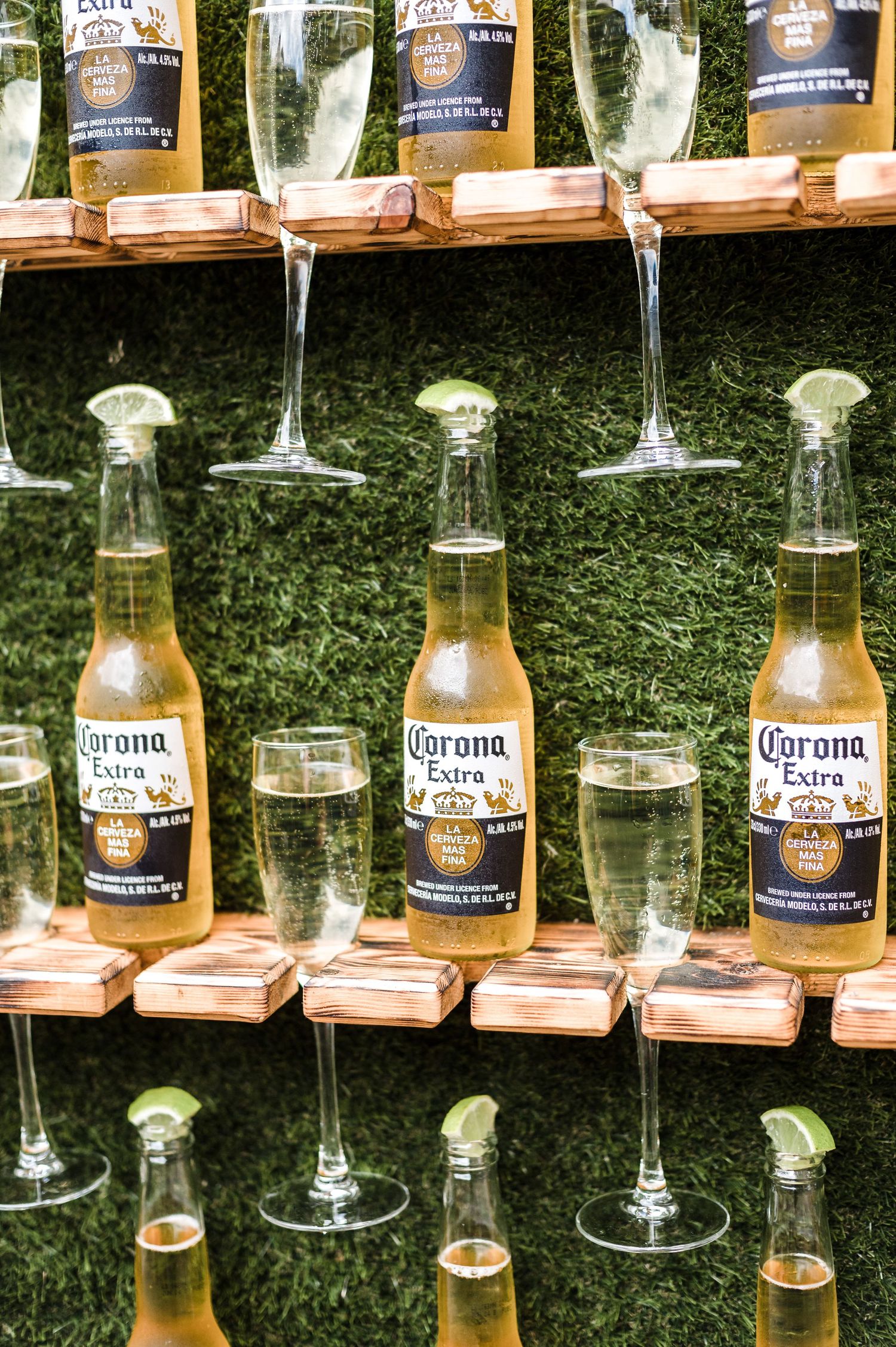 Corona beer bottles and champagne glasses arranged on wooden holders against artificial grass.