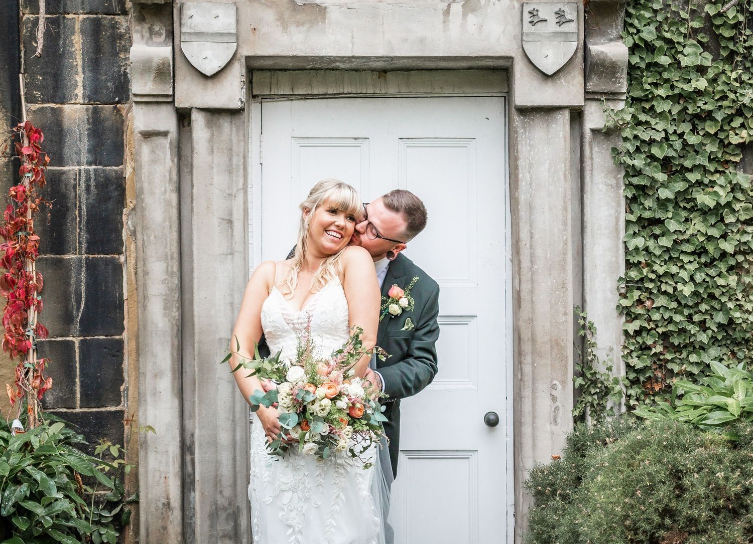 Romantic wedding portrait by an ivy-covered stone doorway with a soft, natural light.
