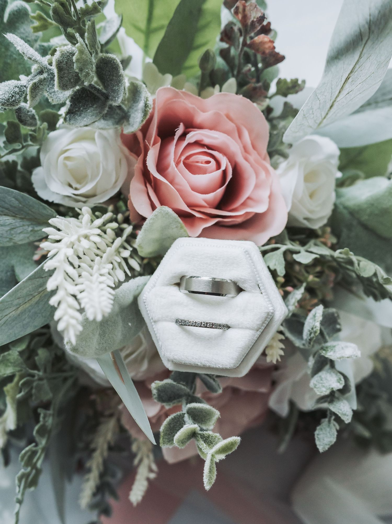 Wedding ring nestled in a white geometric box surrounded by pink and white roses.