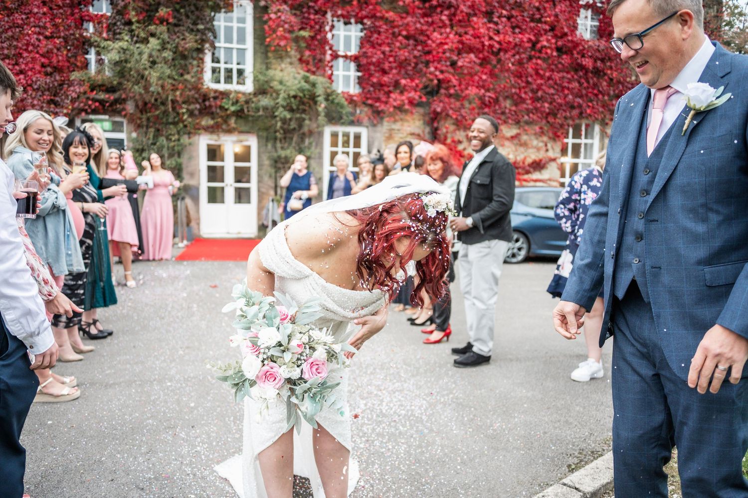 Wedding celebrations in front of a red ivy-covered building with guests looking on.