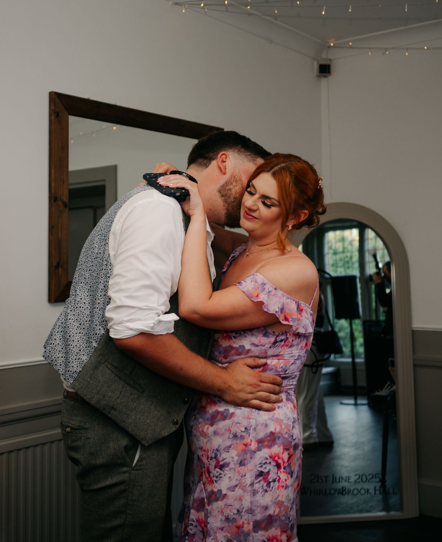 A loving couple share an intimate moment while dancing in a room adorned with string lights.