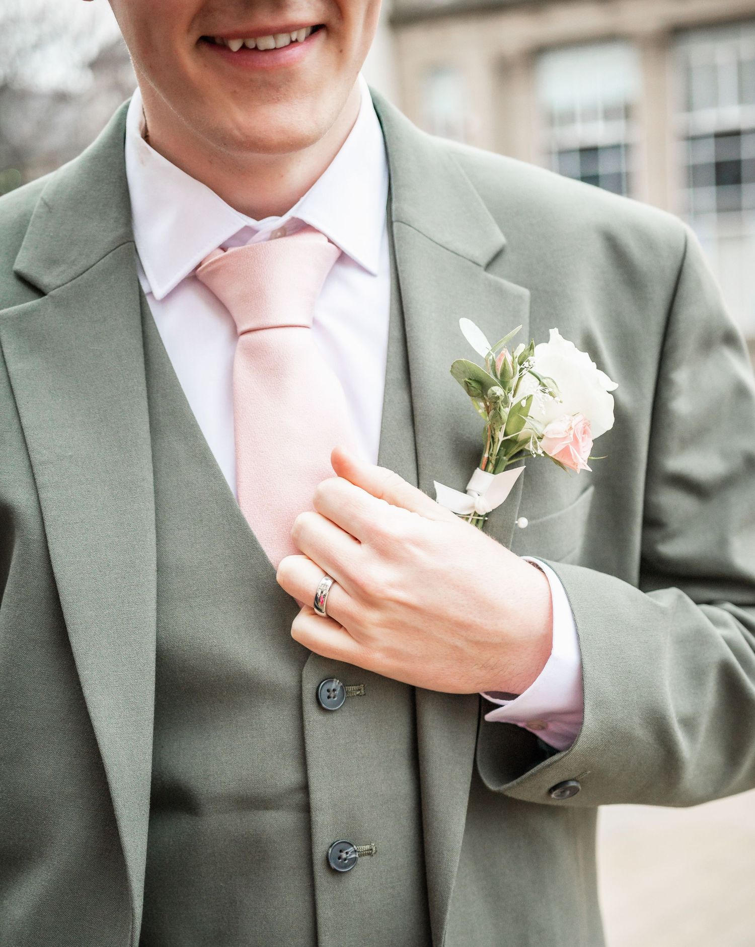 Close-up detail of a sage green suit with pink tie and white boutonniere.