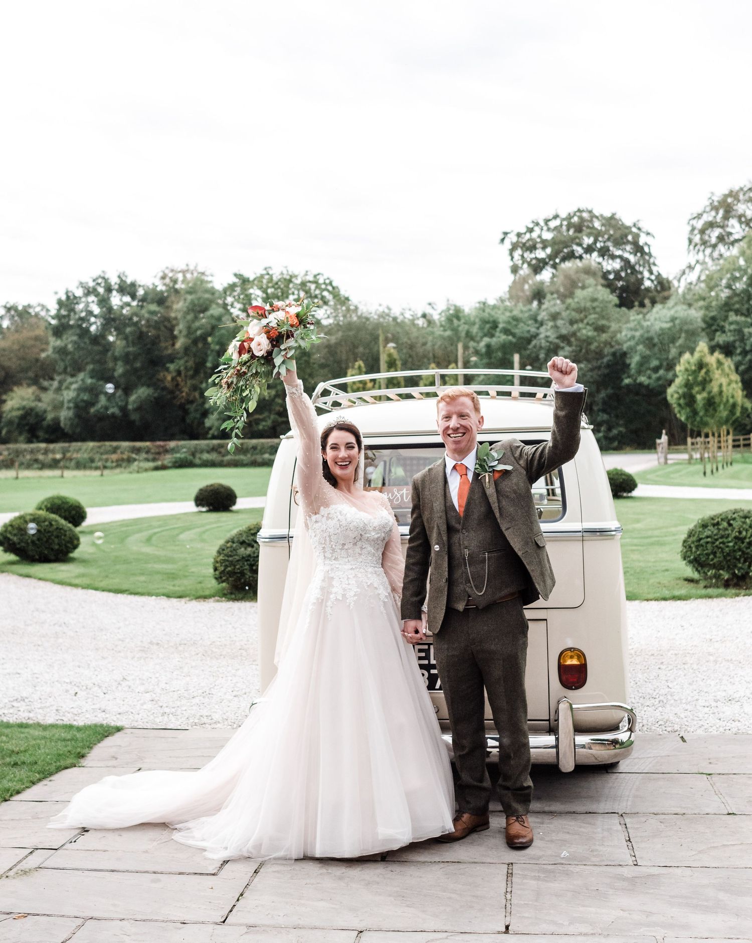Newlyweds celebrating in front of vintage white van in garden setting.