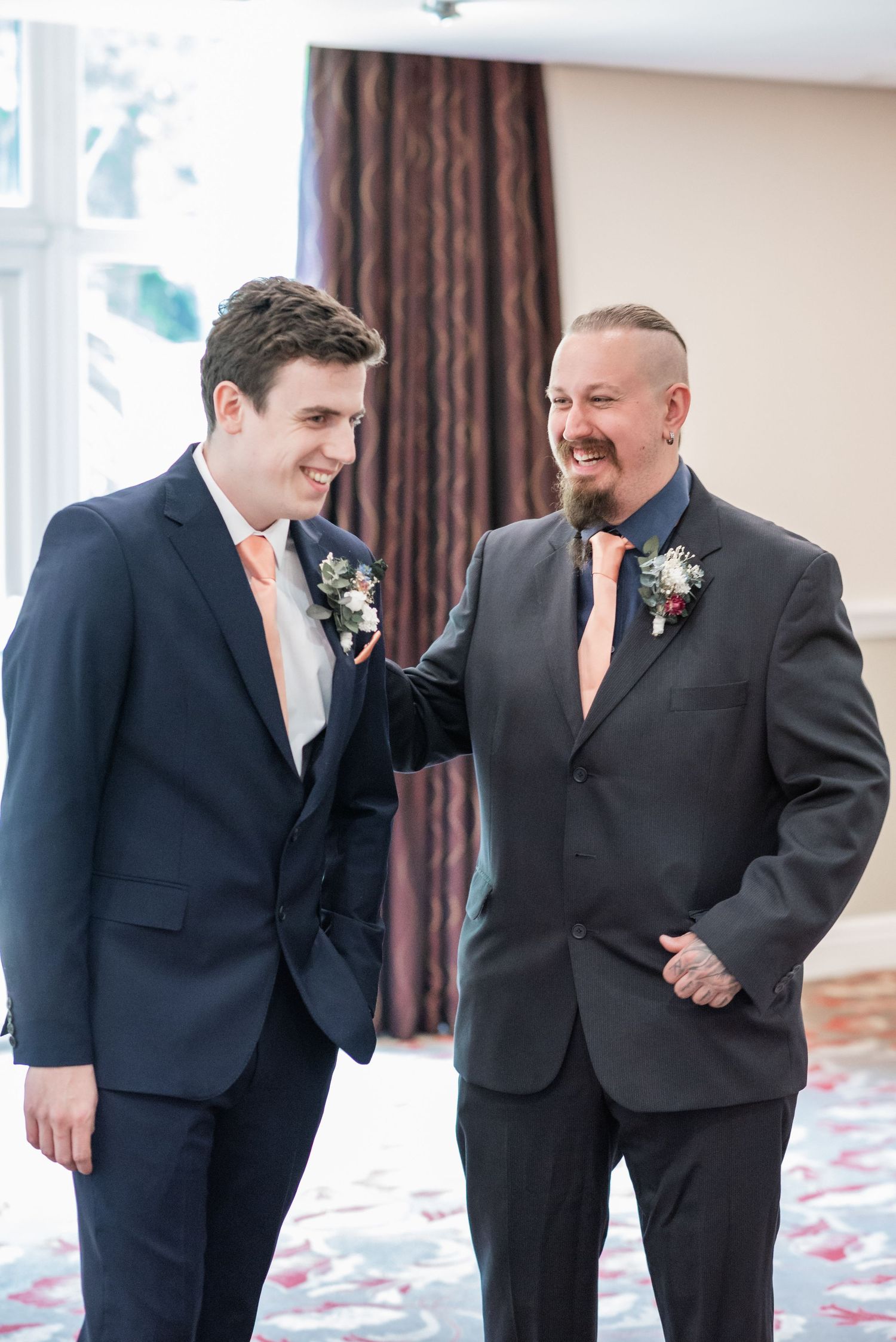Two men in formal suits sharing a moment at wedding celebration.