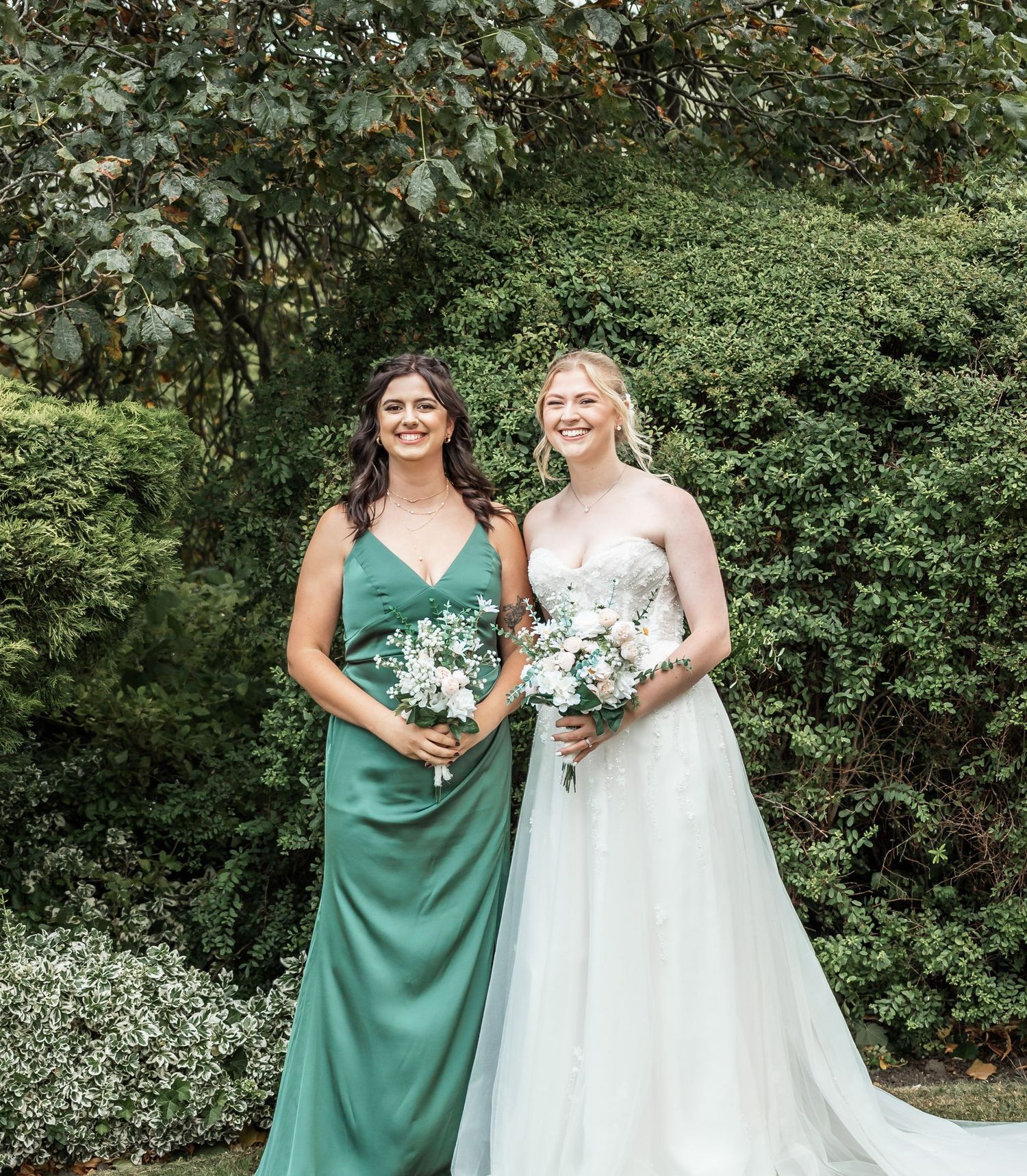 Wedding portrait in a garden setting with bridesmaid in emerald dress.
