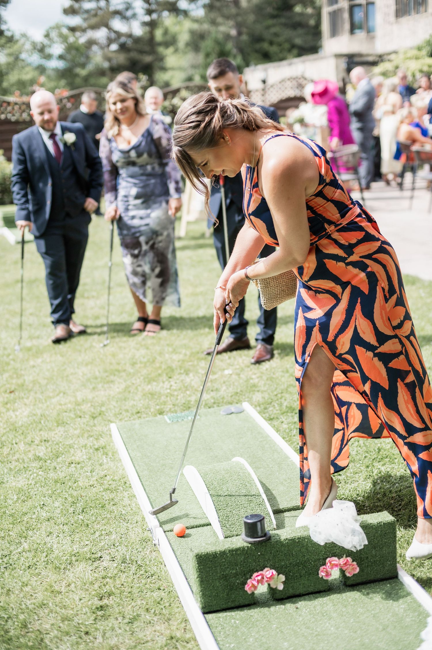 Guest playing mini golf at wedding reception in patterned orange dress and white sneakers.