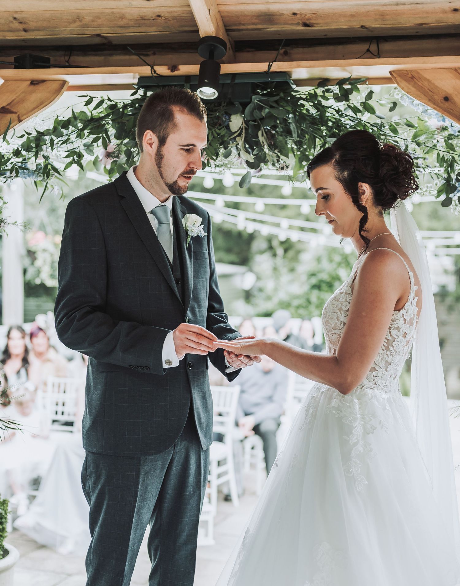 A romantic wedding ceremony takes place under a wooden gazebo decorated with greenery.