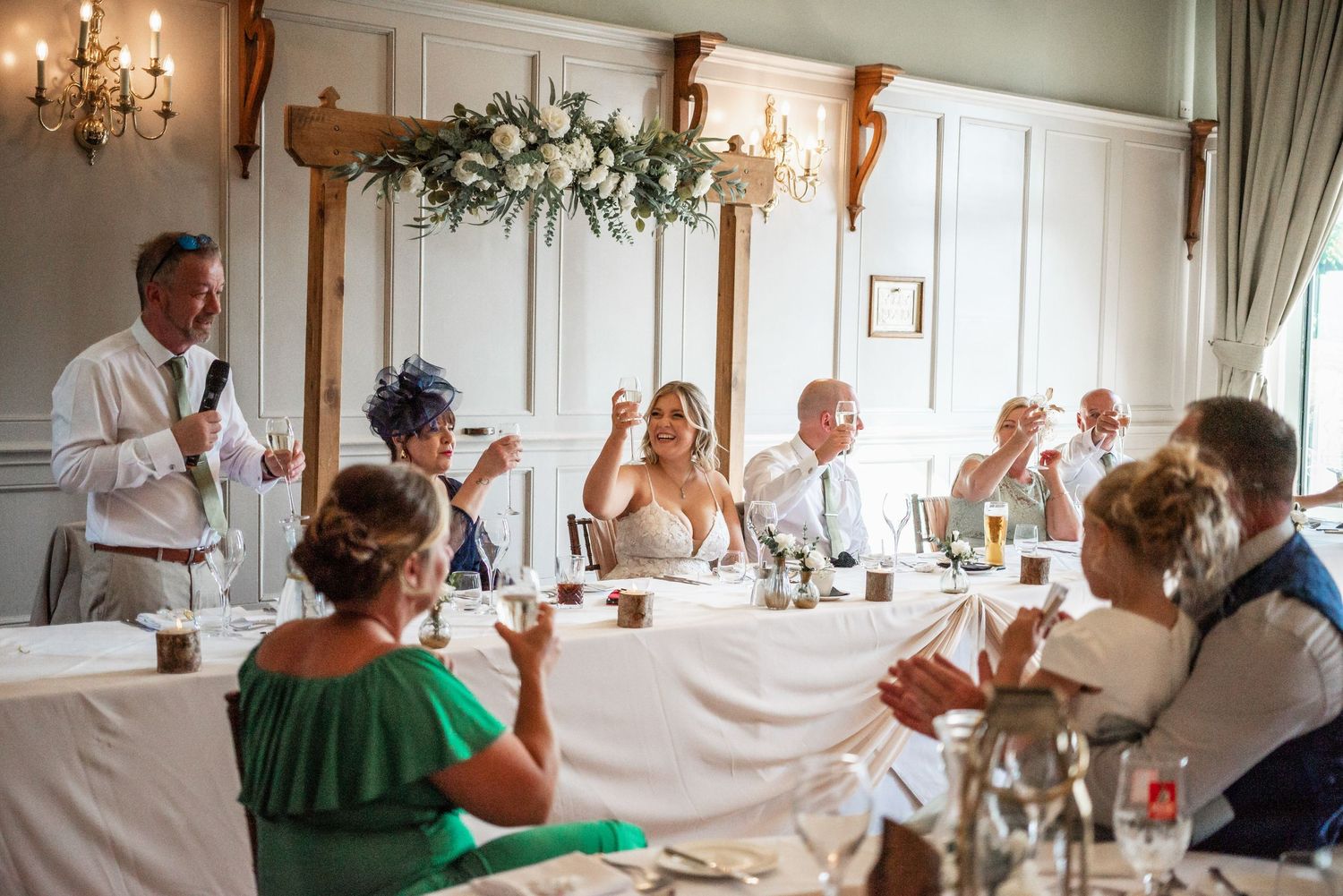 Wedding reception scene with elegant table settings and floral decor during toasts.