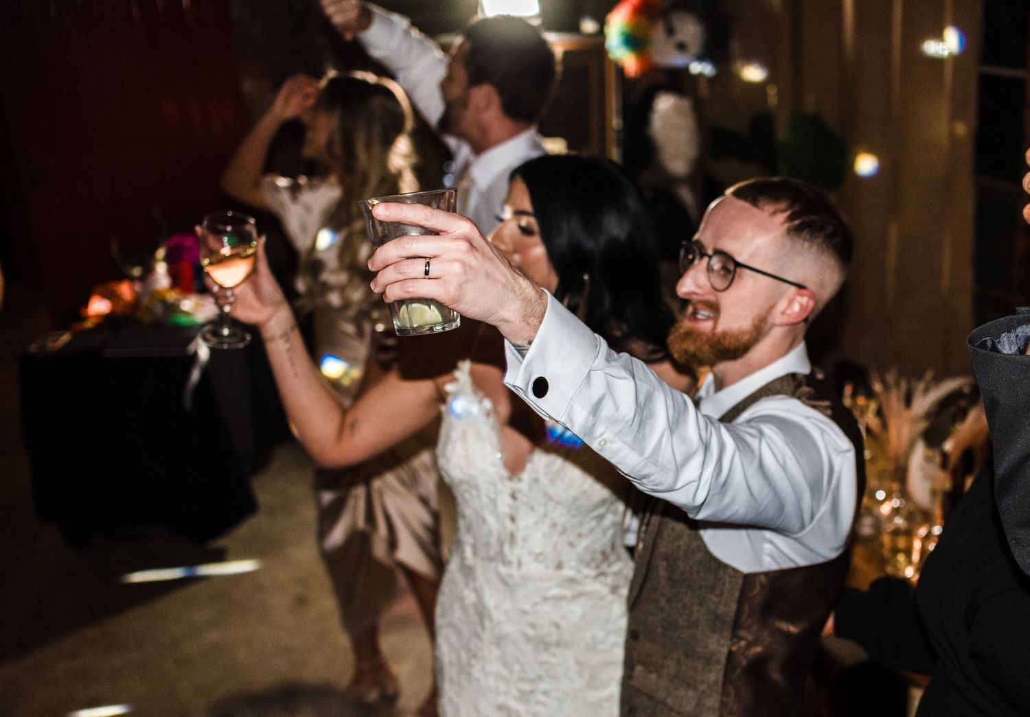 Wedding guests raise their drinks in celebration at rustic venue.