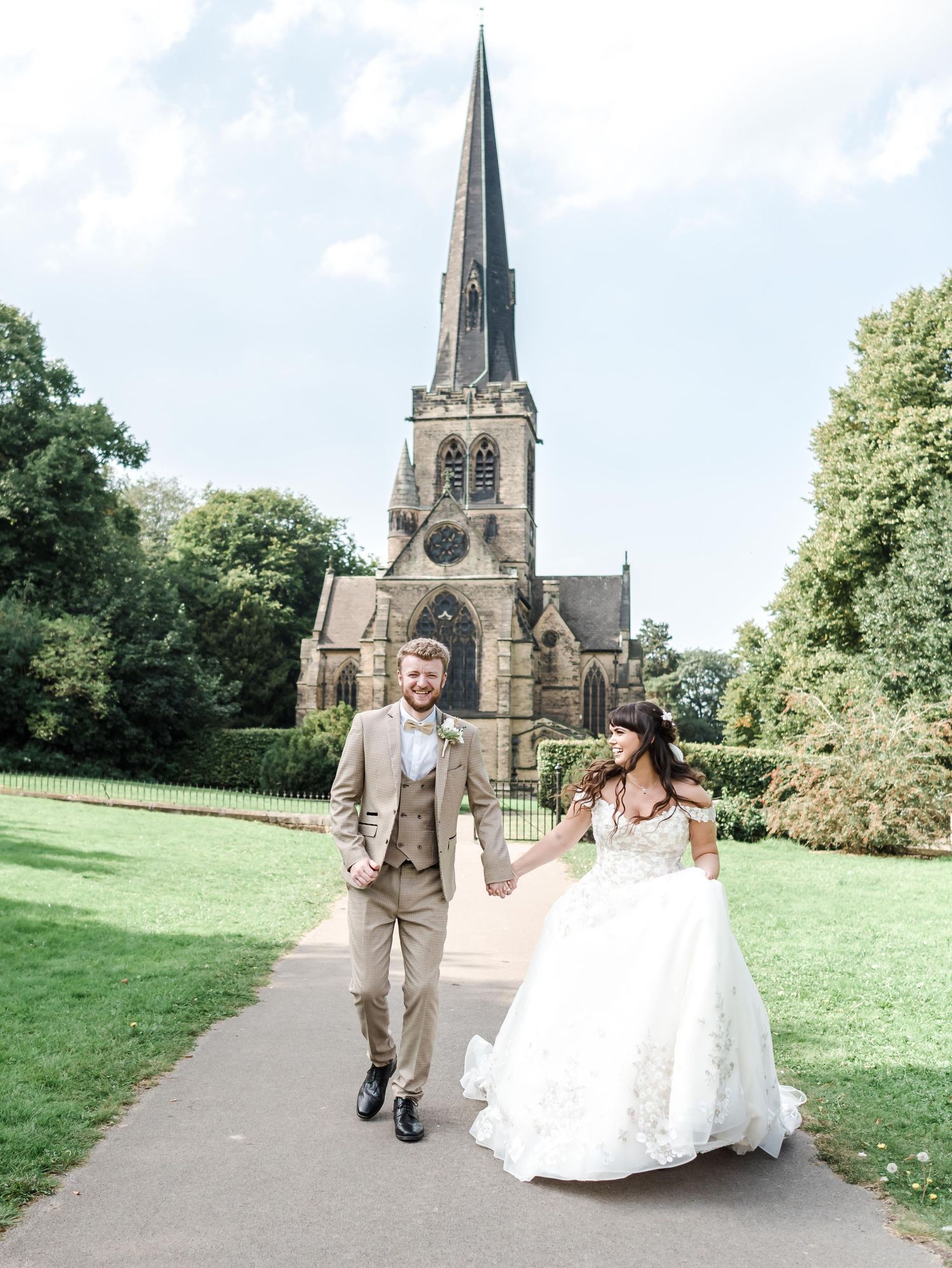 Elegant couple walking hand in hand in front of a grand stone church with tall spire.
