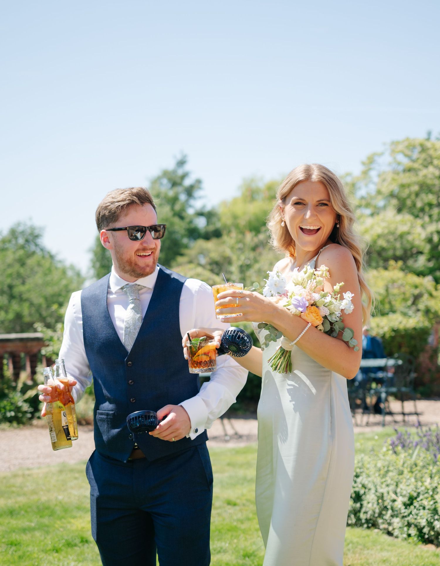 Wedding couple enjoying drinks together in a sunny outdoor garden setting.