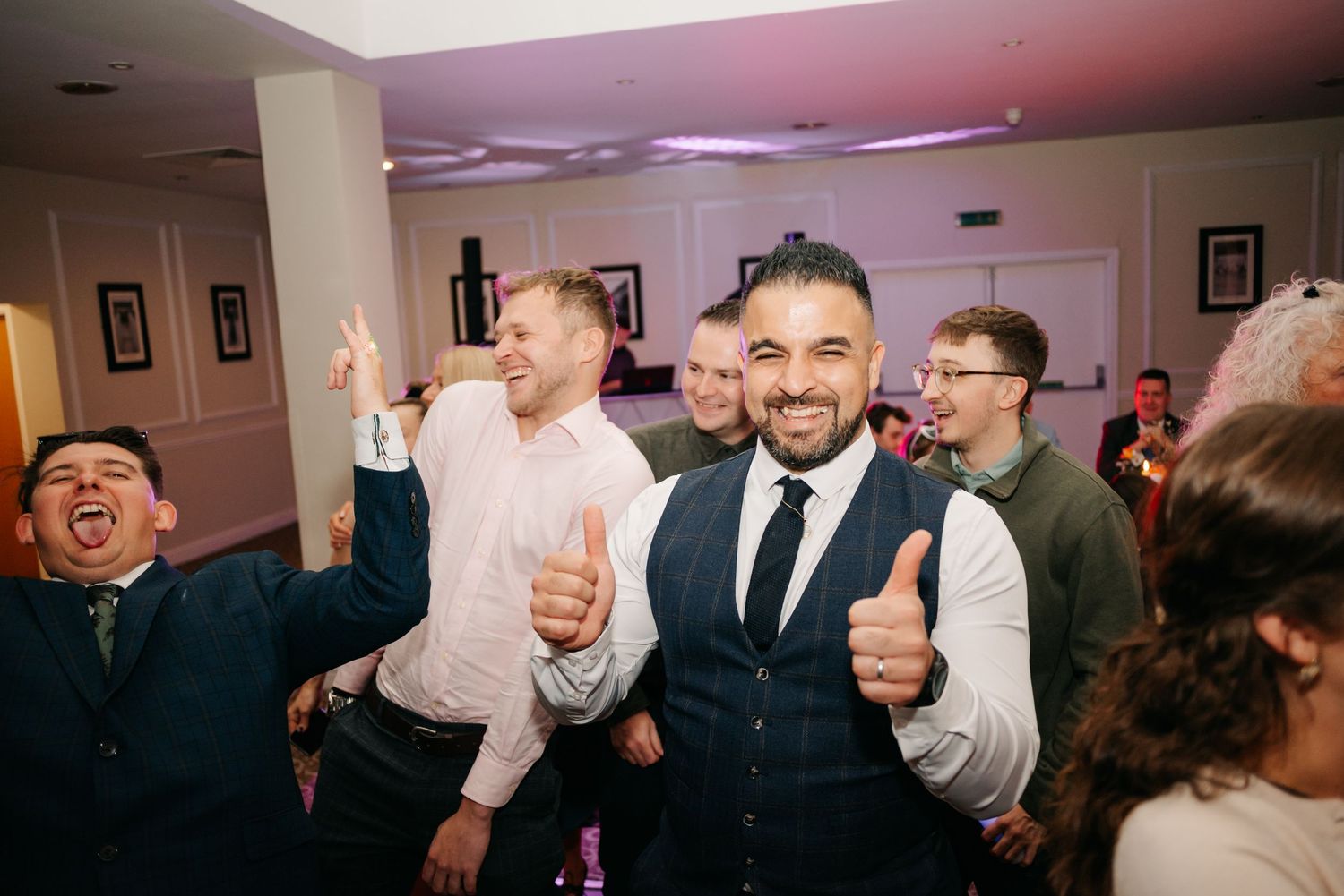 Wedding guests dancing and celebrating at an indoor reception party.