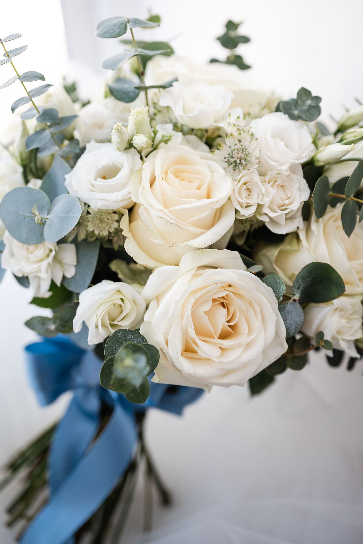 Elegant white rose wedding bouquet with eucalyptus greenery and navy blue ribbon tied around stems.