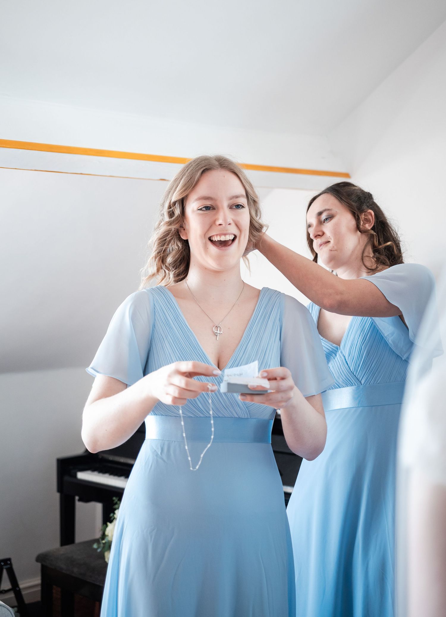 Two bridesmaids in light blue dresses share a joyful moment while getting ready for the wedding.