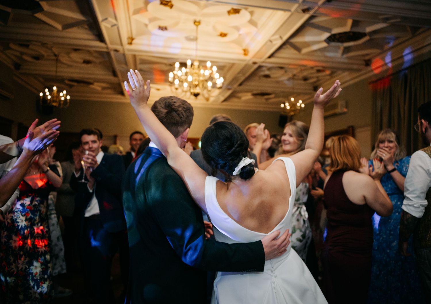 Wedding reception dance floor filled with celebrating guests under crystal chandeliers.