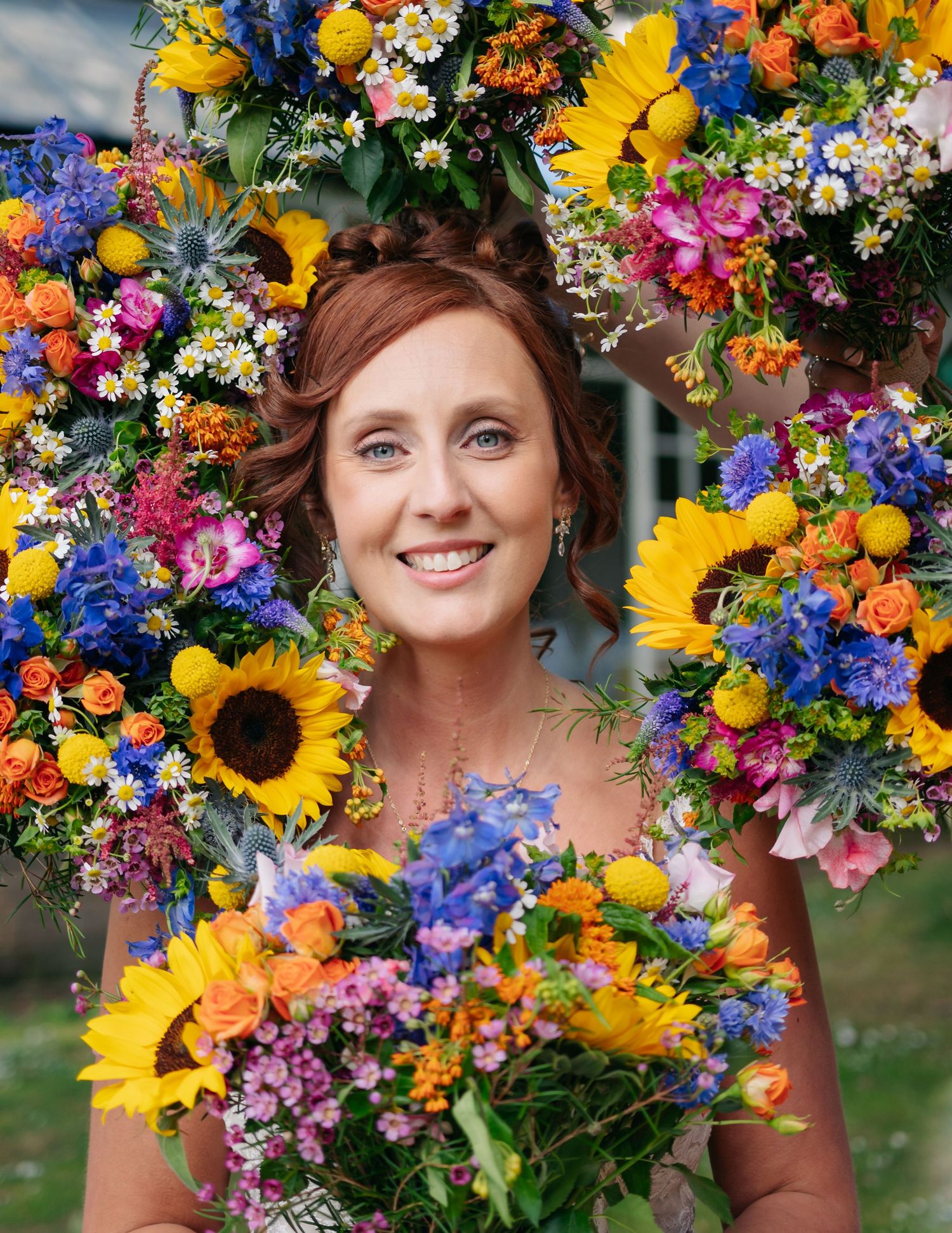 Vibrant wedding bouquet featuring sunflowers, blue delphiniums, and colorful wildflowers arranged in rustic style.